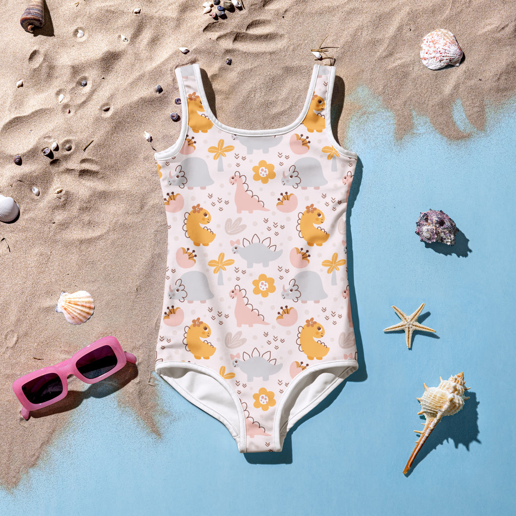 A playful off-white girls one-piece swimsuit with yellow and pink dinosaur print and orange flowers with UPF 50+ protection