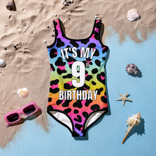 A vibrant girls one-piece swimsuit with rainbow leopard print and bold white text its my 9th birthday