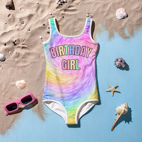 A vibrant rainbow tie dye girls one piece swimsuit with birthday girl in colorful outlined letters on the chest