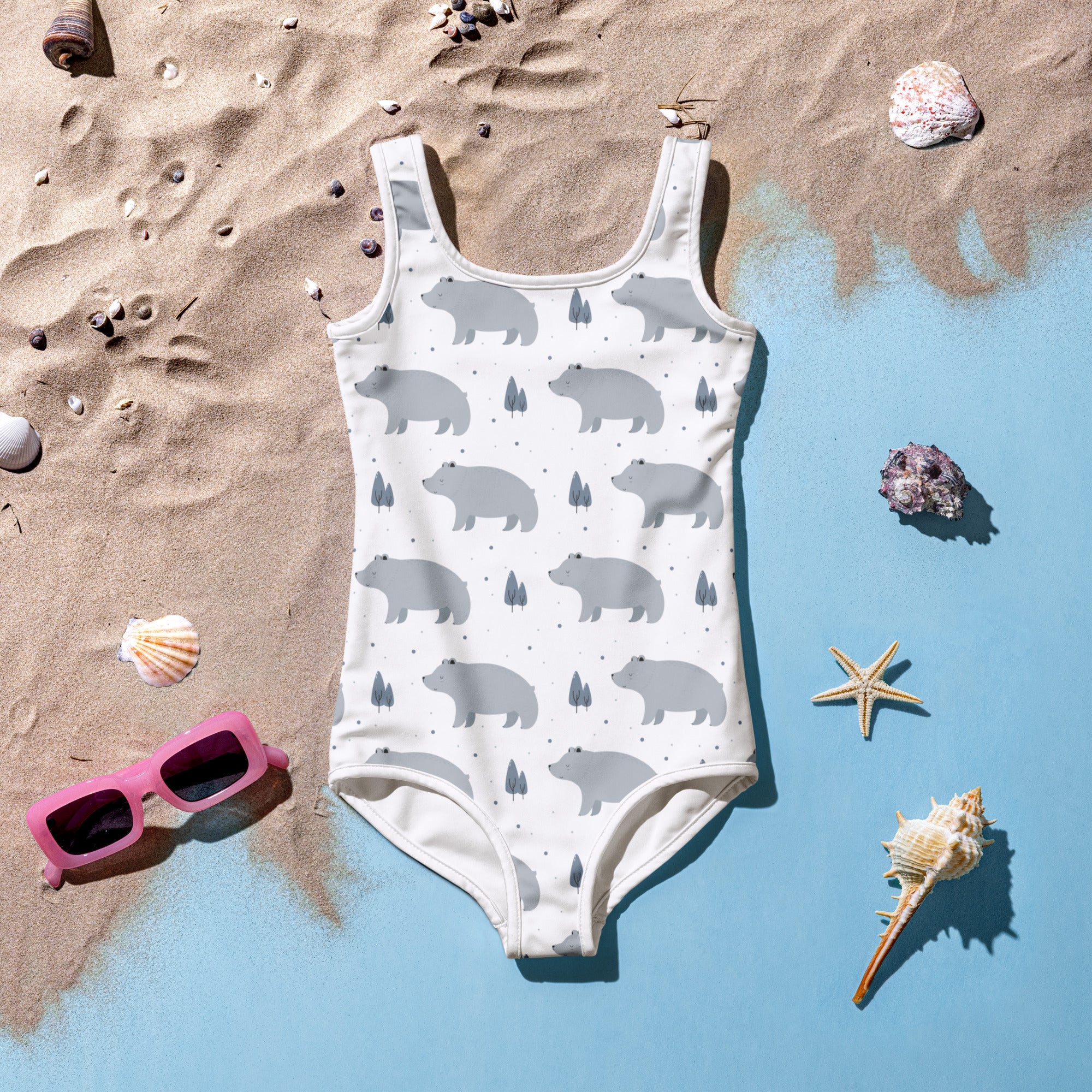 Girls polar bear buttery soft white one-piece swimsuit with gray pattern and upf 50 plus laid on sandy beach decor