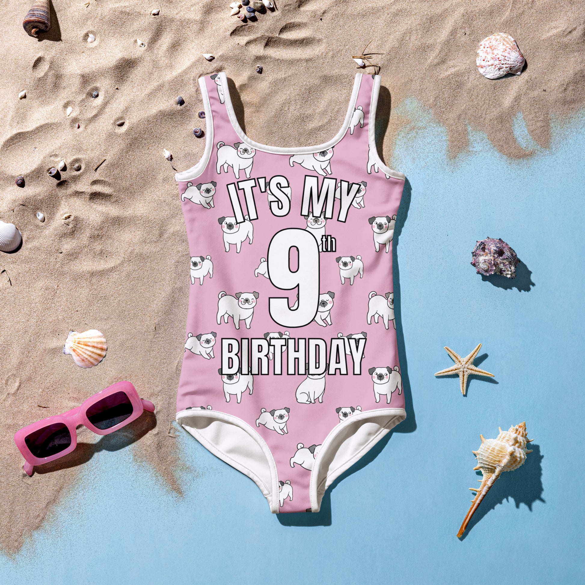 Girls pink swimsuit with 'It's My 9th Birthday' text on a sandy background with shells and sunglasses.