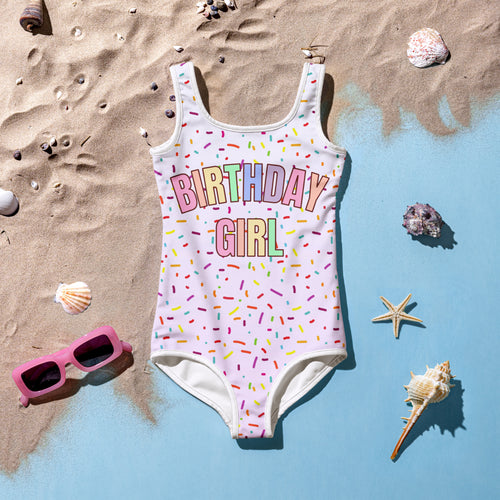 A white one-piece buttery soft swimsuit with colorful sprinkles and rainbow birthday girl print for celebrations