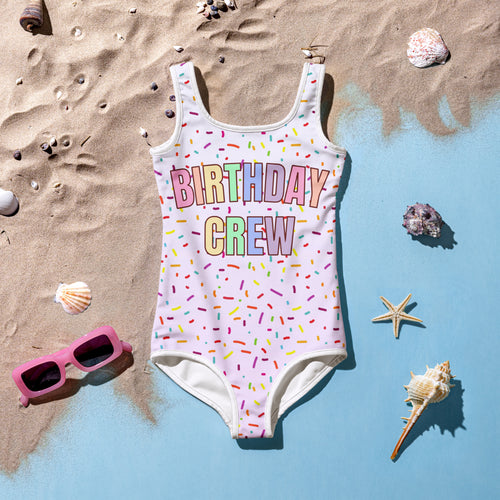 White buttery soft one-piece swimsuit with birthday crew rainbow print and colorful sprinkle patterns for birthdays