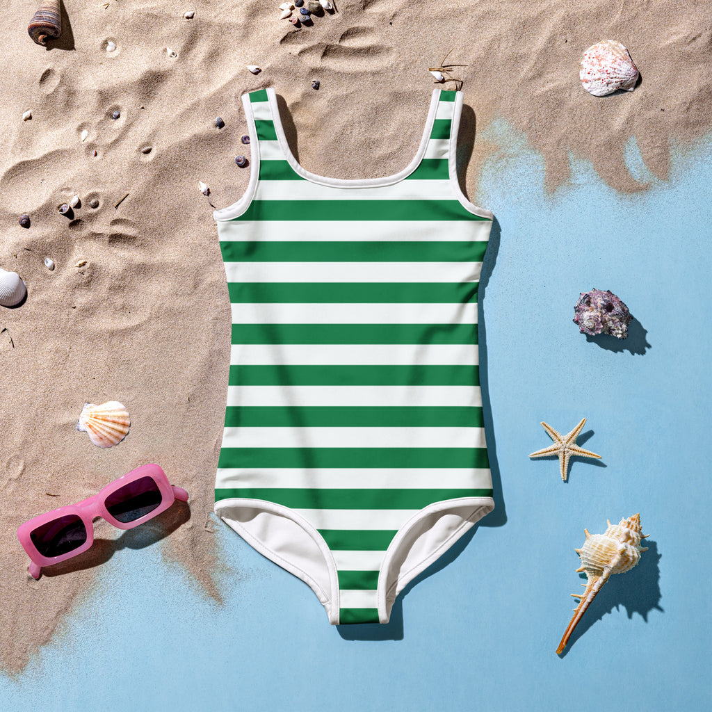 Girls green and white buttery soft one-piece swimsuit with UPF 50 plus laid flat on sand beside seashells