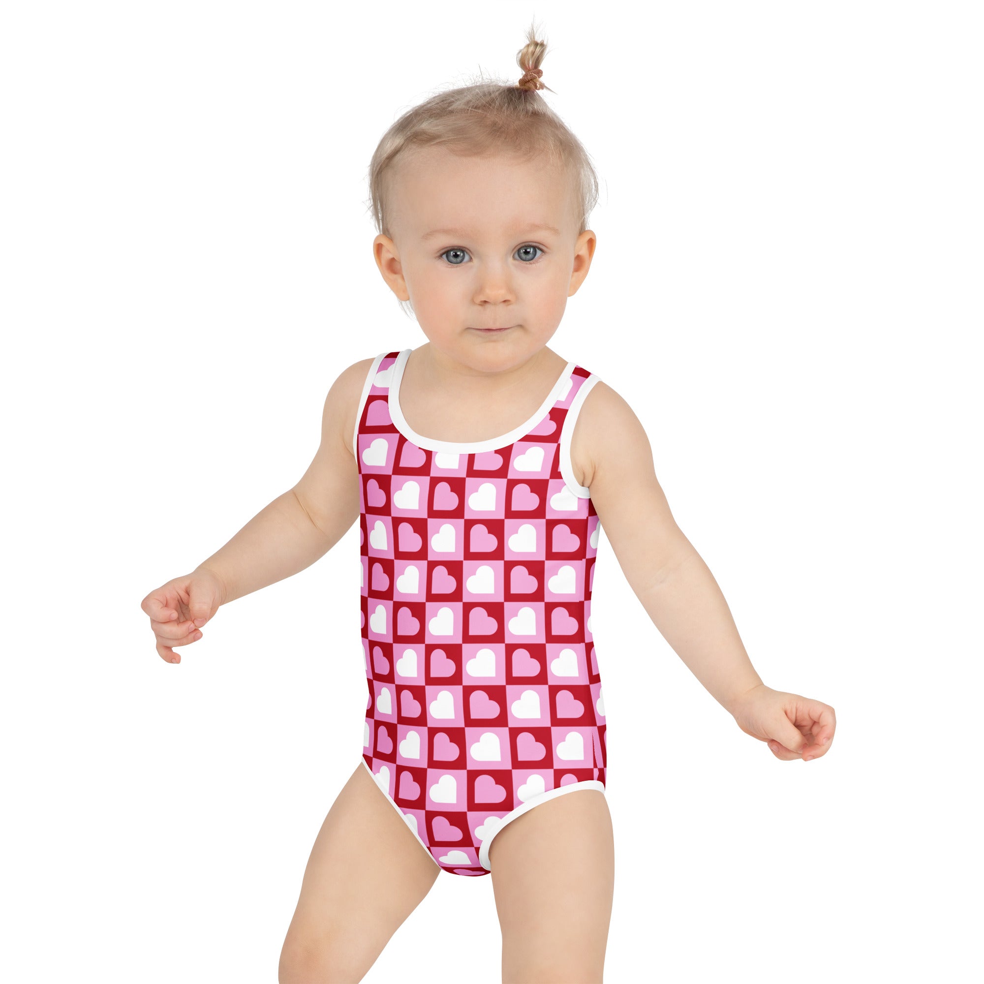 A toddler wears a girls pink heart squares checkerboard buttery soft swimsuit with UPF 50 plus and double layered front