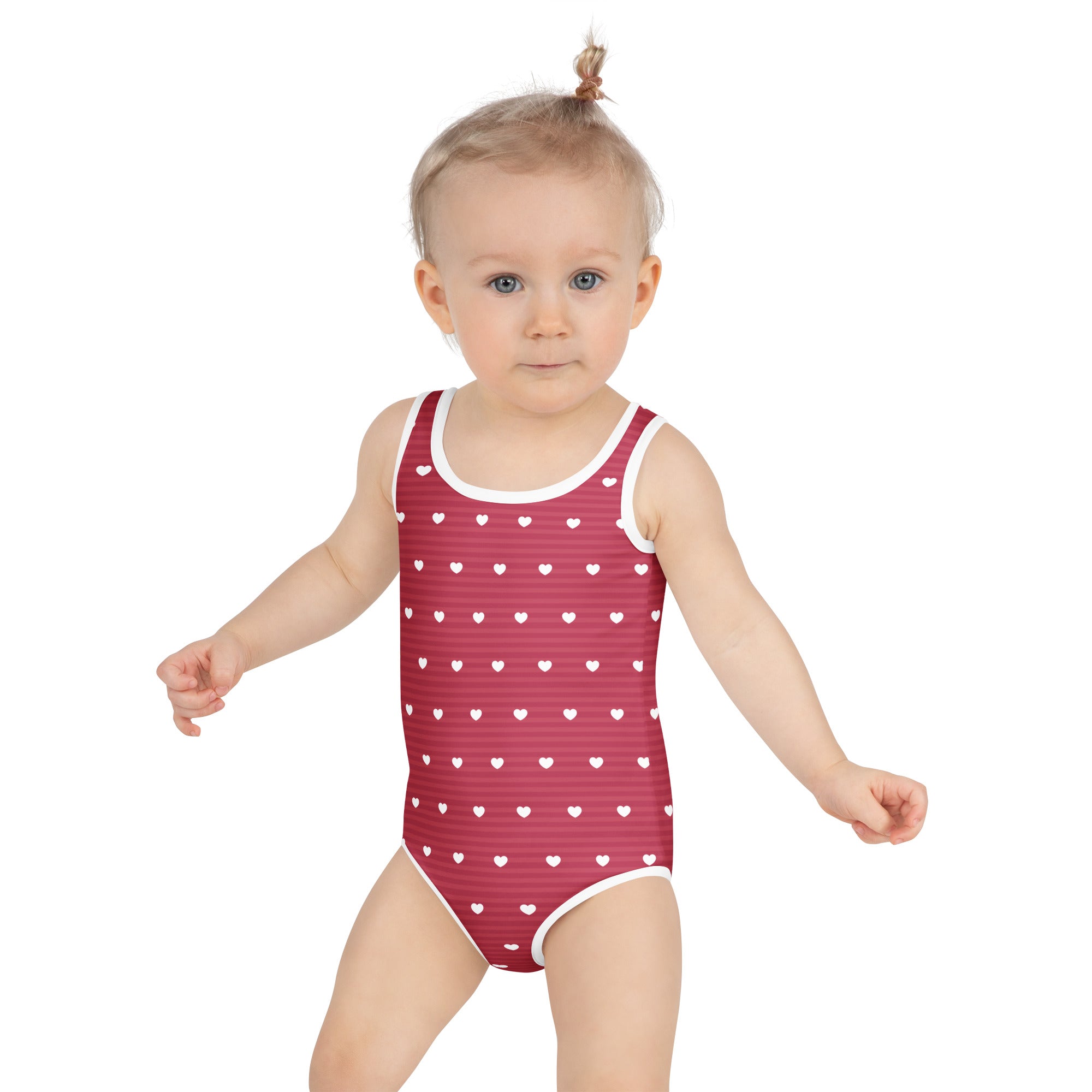 A child wearing a red girls heart stripe buttery soft swimsuit with white hearts and UPF 50 plus protection