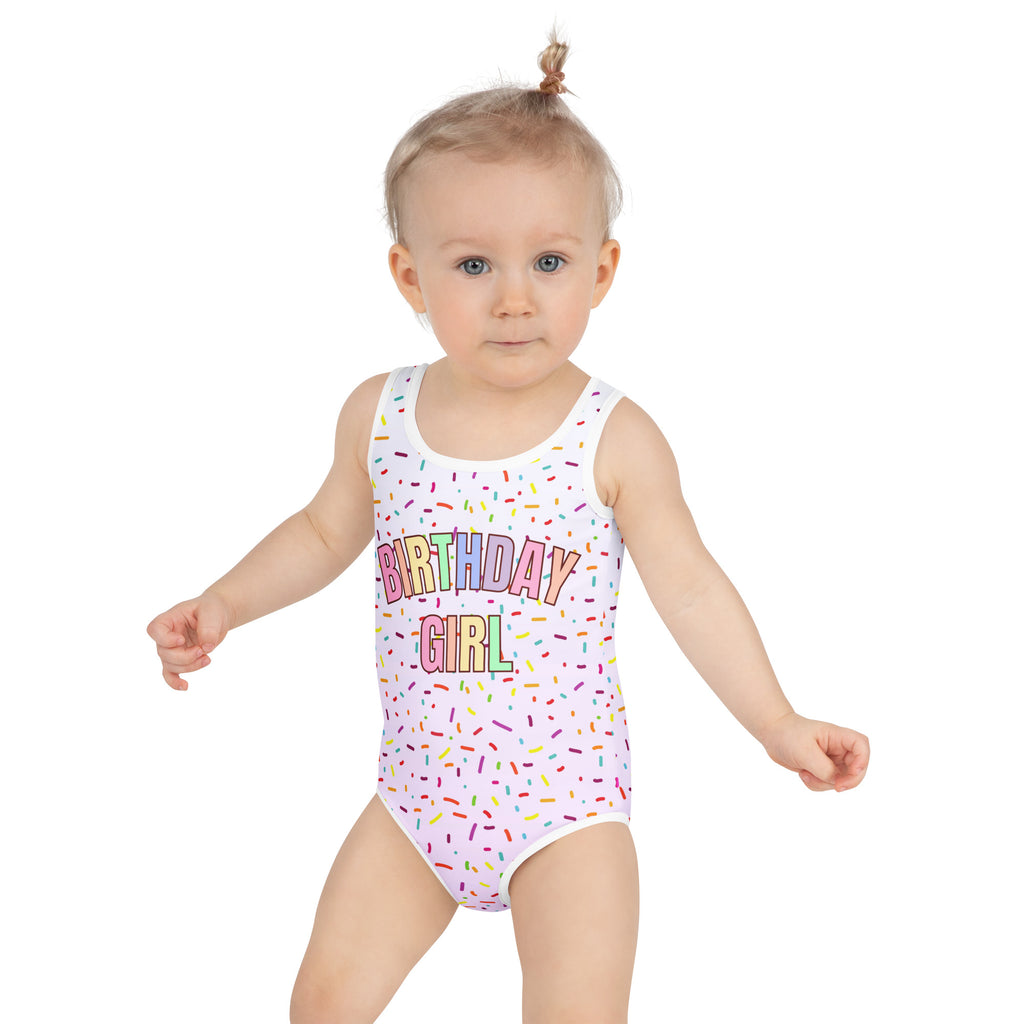 Child wearing a 'Birthday Girl' swimsuit with colorful text and sprinkles on a white background