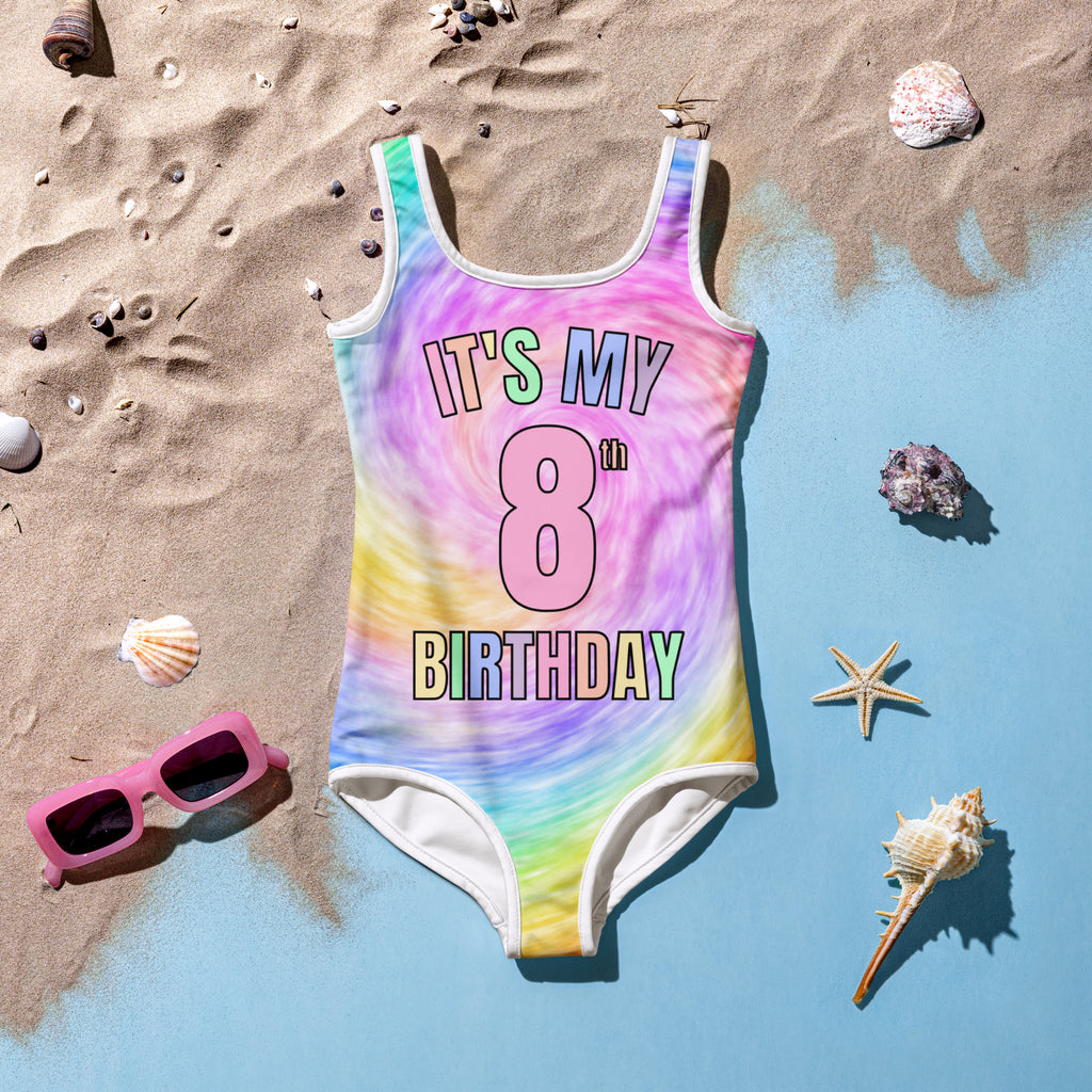 Colorful swimsuit with 'It's My 8th Birthday' text on a beach setting with shells and sunglasses.