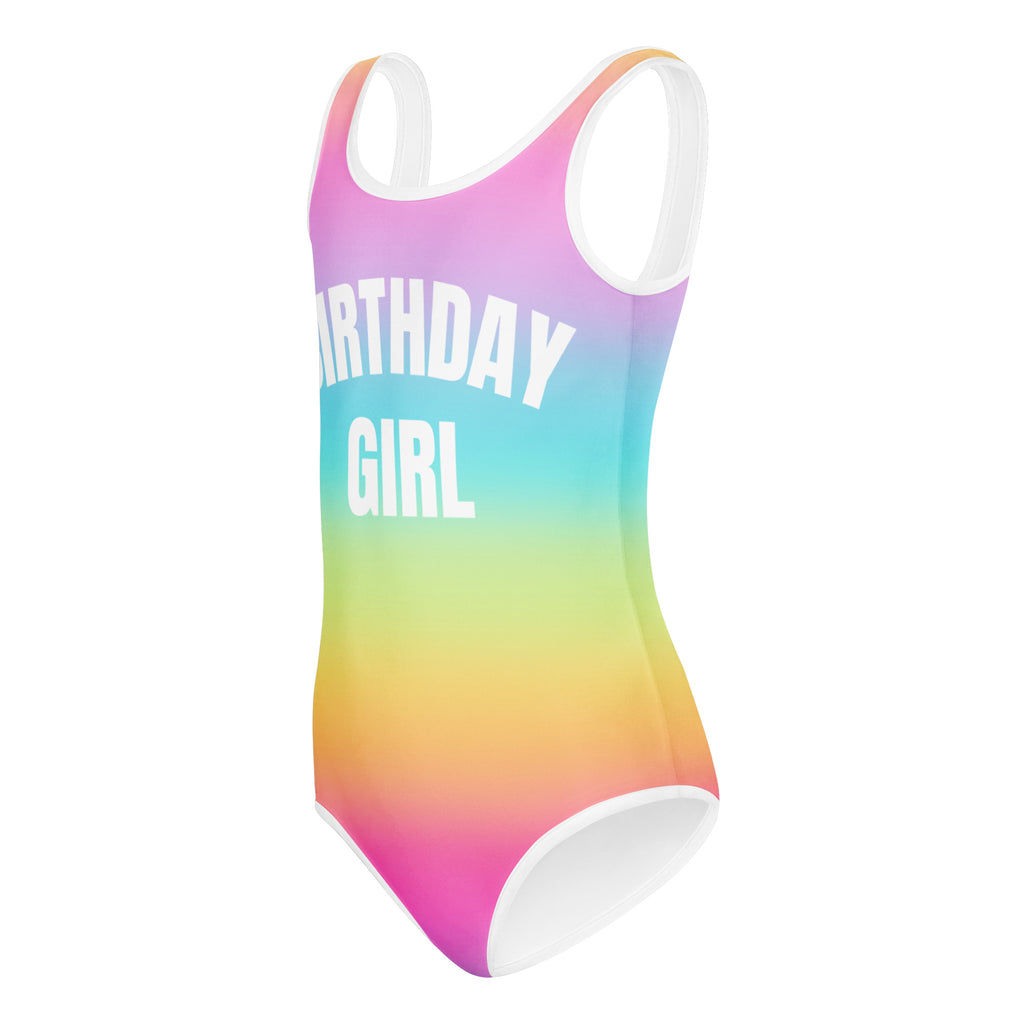 A vibrant rainbow gradient buttery soft one-piece swimsuit with white trim and birthday girl print for dance and gymnastics