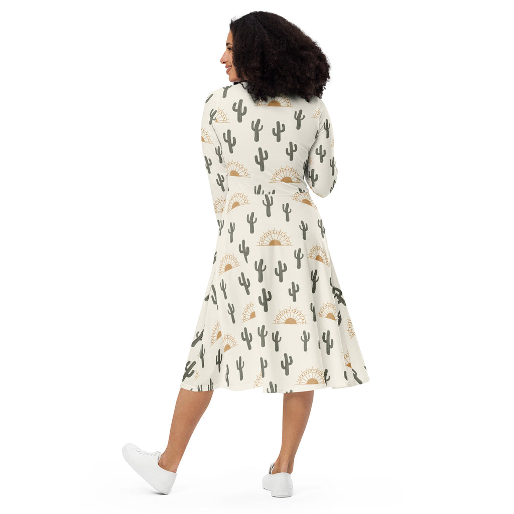 Women’s off-white a-line midi dress with long sleeves featuring black and gold cactus and sun patterns with pockets