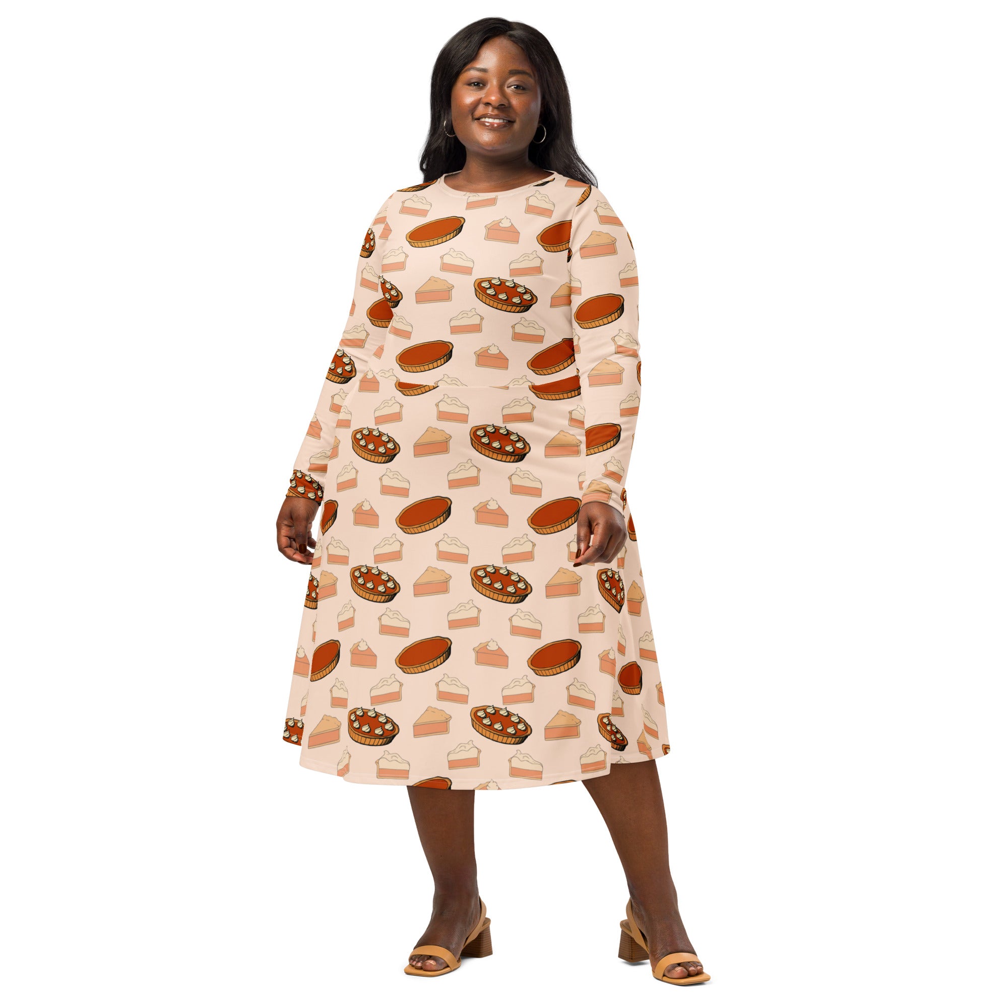 A plus-size woman wears a soft peach long-sleeve midi dress with illustrated pumpkin pies and pockets