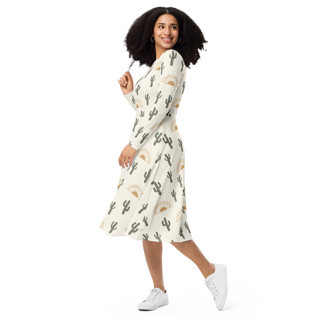 A woman wearing a cream-colored long sleeve midi wrap dress with black cactus and gold sunburst patterns and pockets