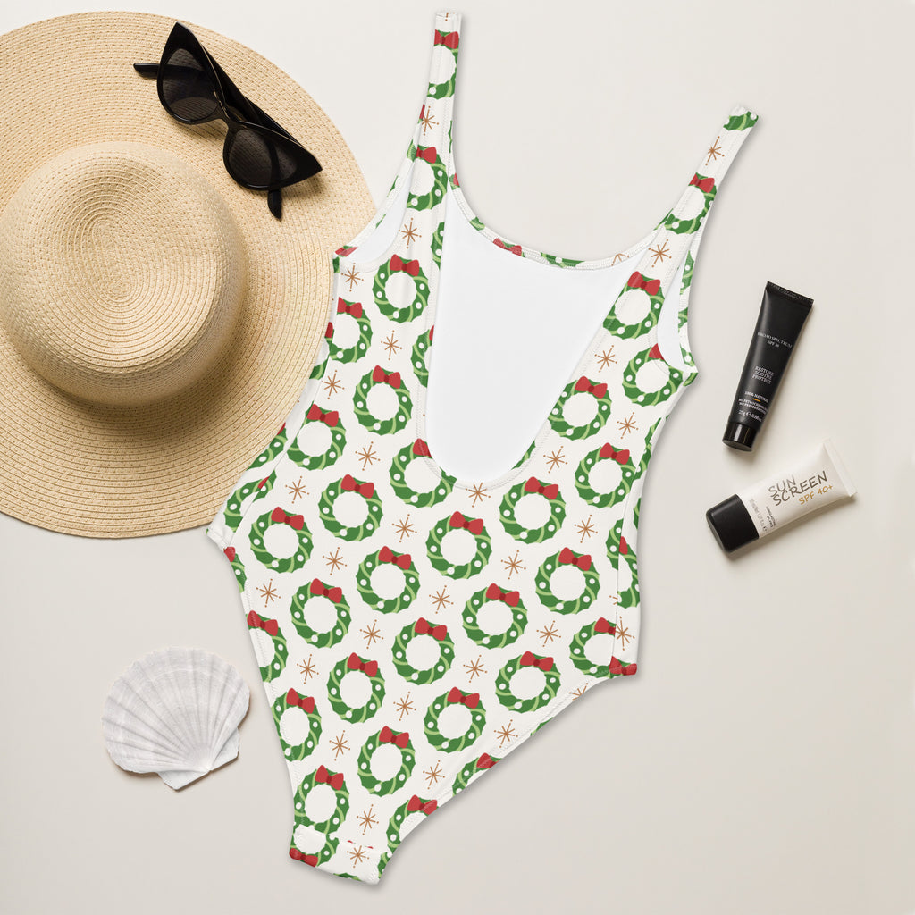 White buttery soft one-piece swimsuit with festive green wreaths red bows gold starbursts and upf 50 plus protection