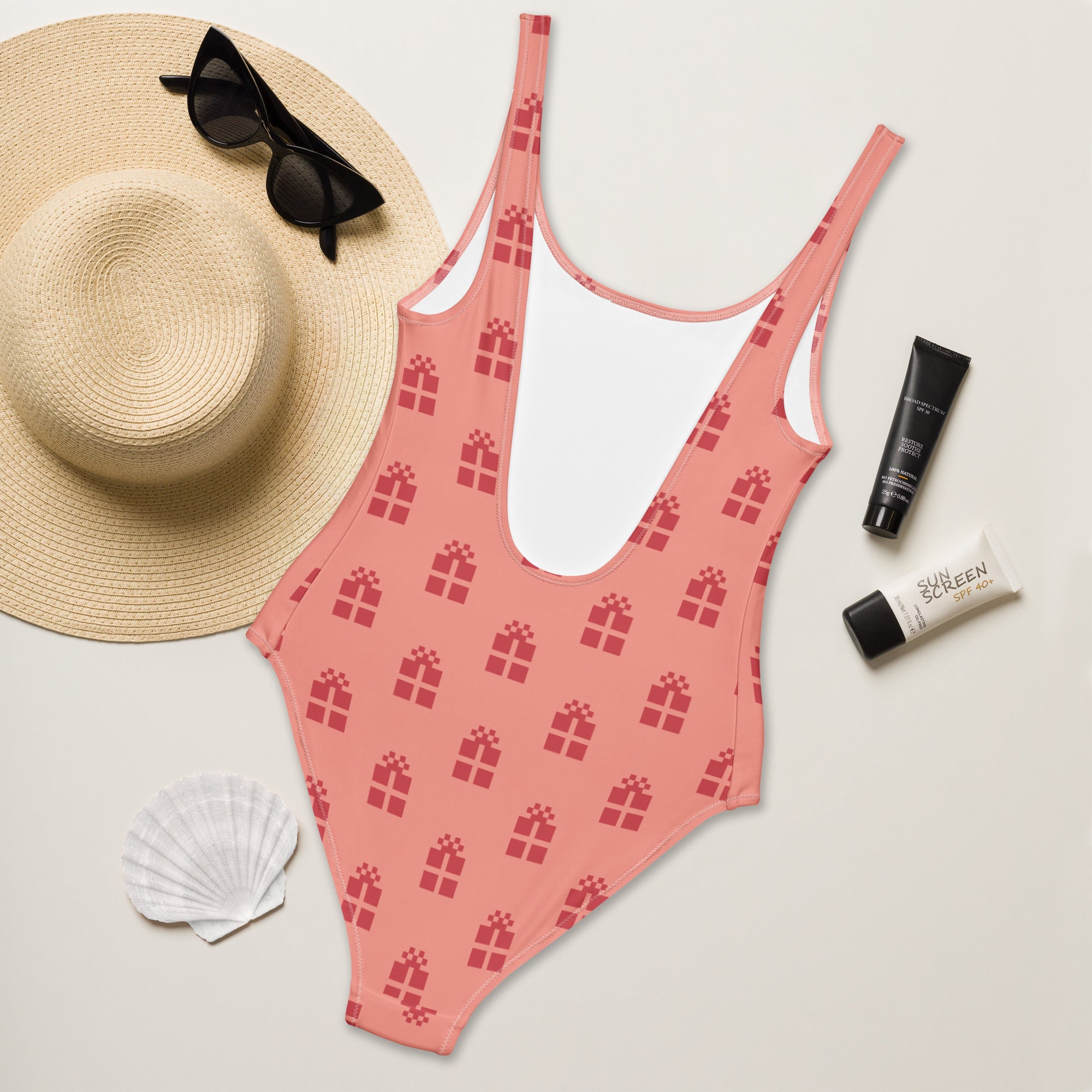 A pink womens christmas gift buttery soft one-piece swimsuit with red gift box pattern and white inner lining with UPF 50+
