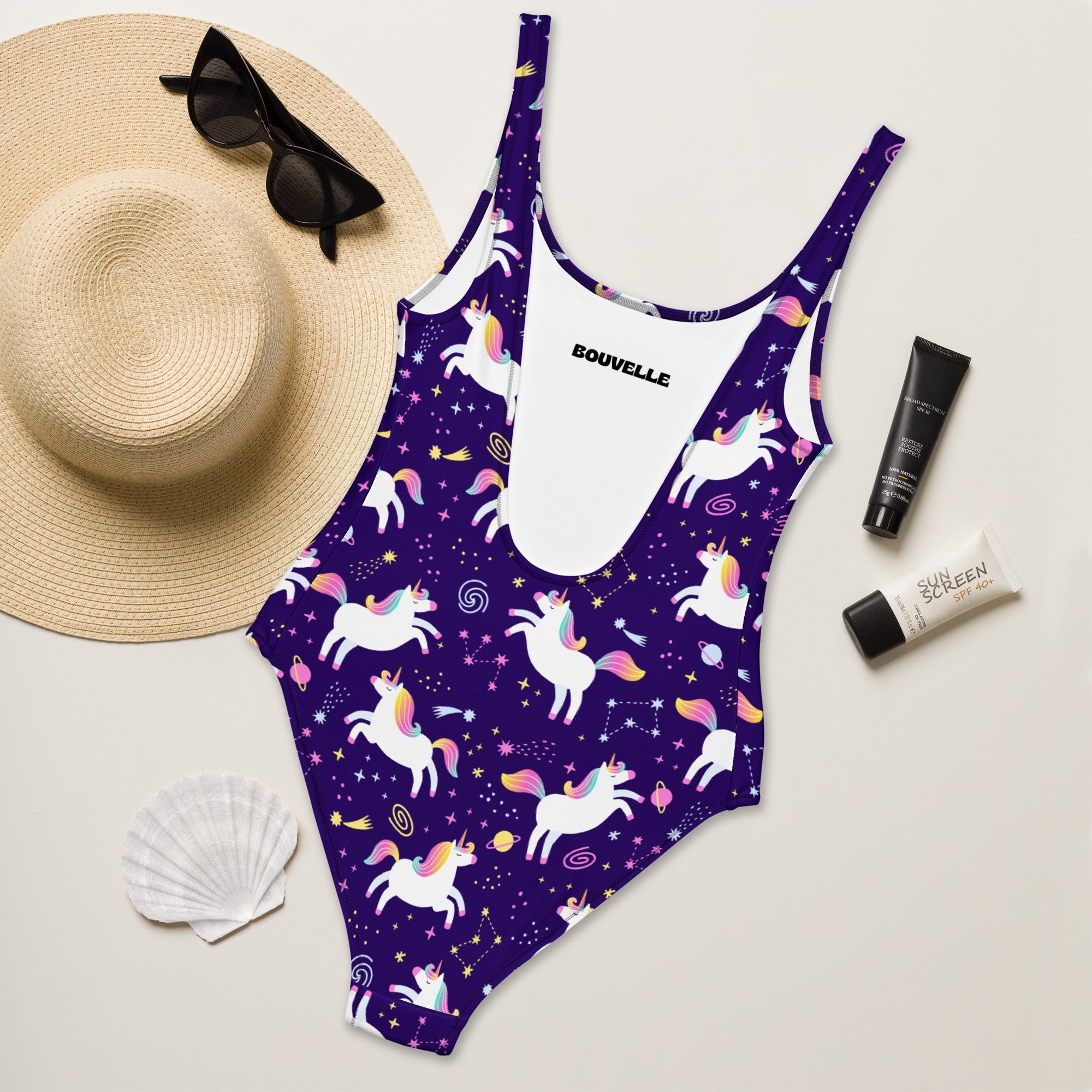 Purple swimsuit with unicorn pattern on a white surface with accessories.