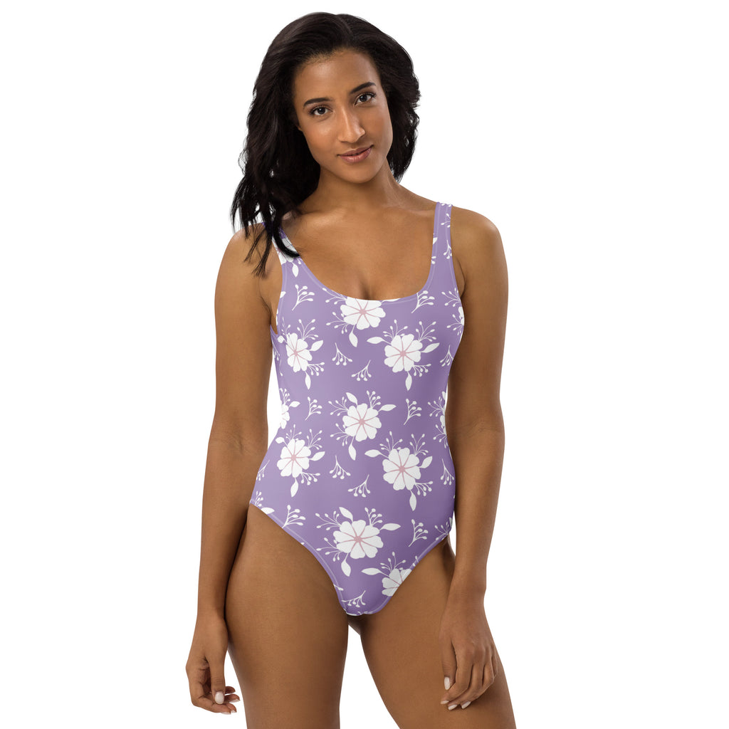 A lavender one-piece swimsuit with a white floral pattern and thin straps featuring buttery soft fabric and UPF 50+ protection