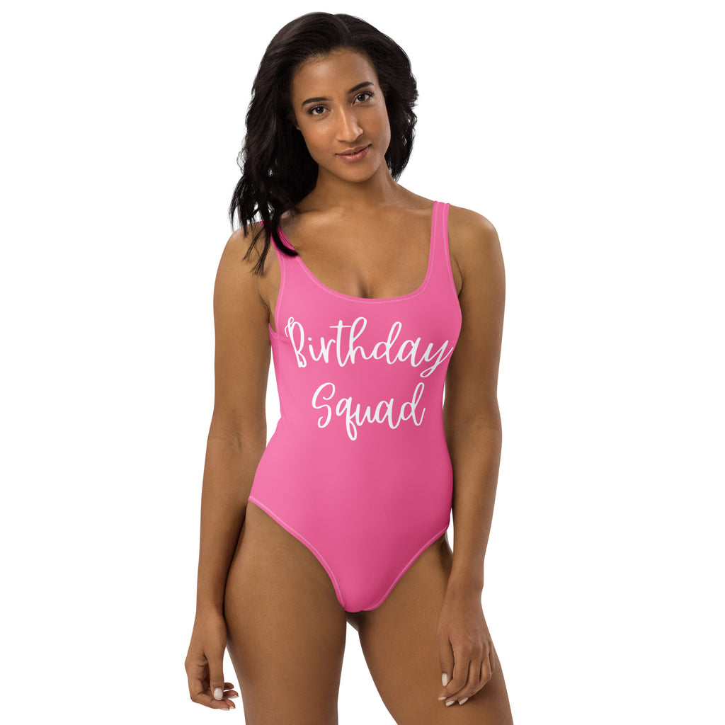 A vibrant pink buttery soft one-piece swimsuit with upf 50+ and birthday squad printed in white cursive across chest