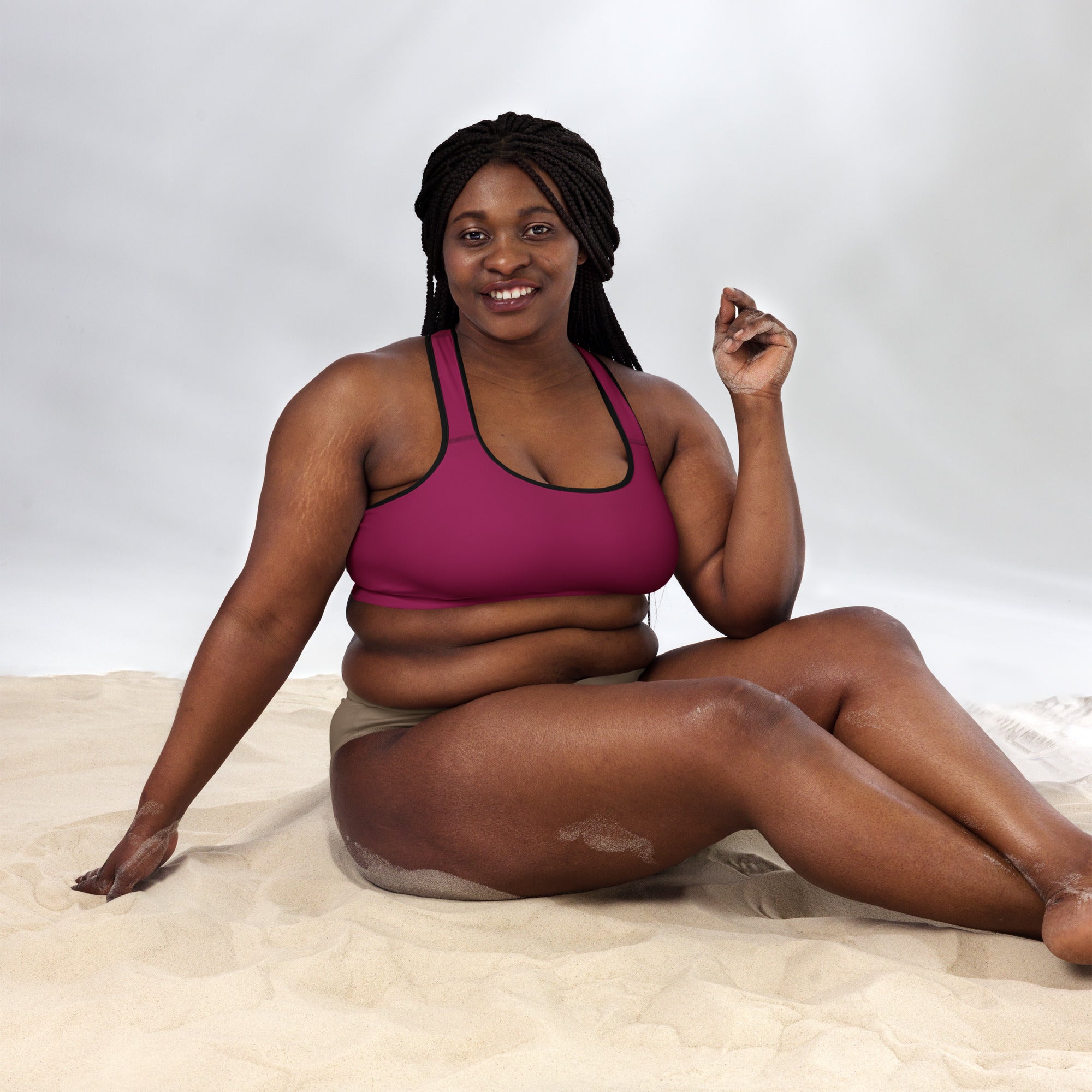 A woman sitting on sand wearing a women’s burgundy padded sports bra with black trim buttery soft quick dry