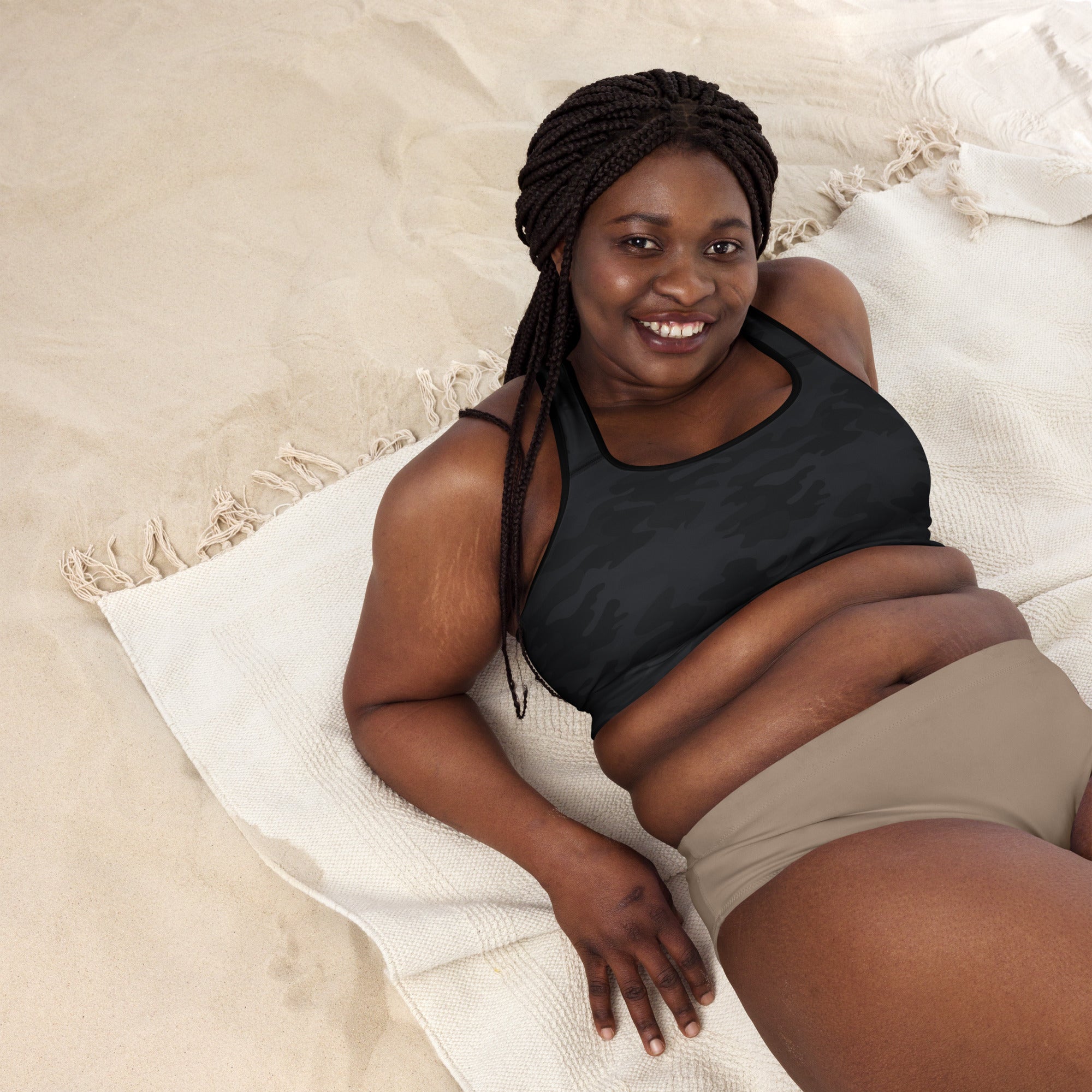 A woman lying on a white towel wearing a women’s black camouflage padded sports bra that is buttery soft and quick-dry
