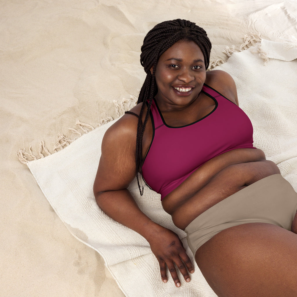 A woman wearing a women’s burgundy padded sports bra in magenta with black trim and beige shorts lying on a towel