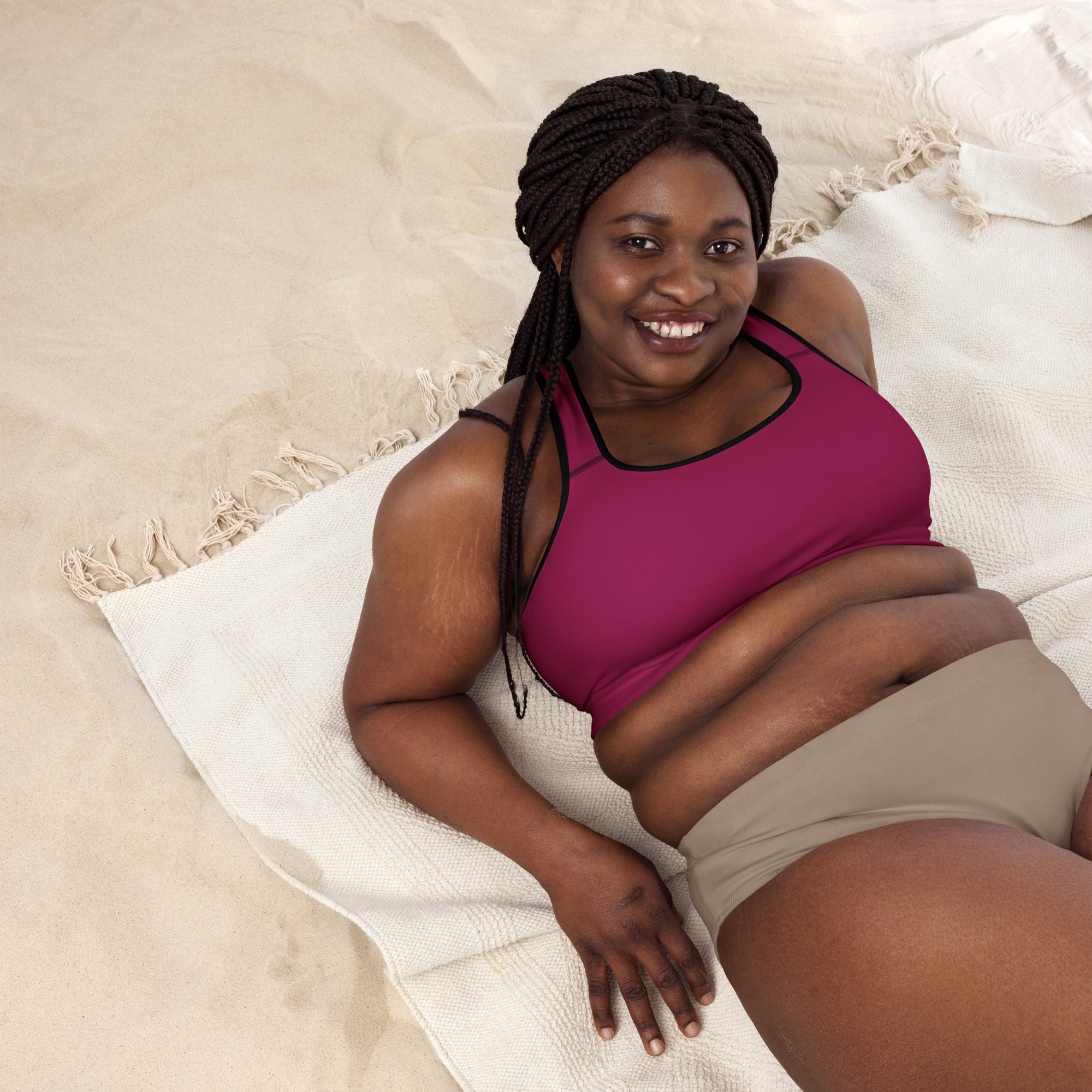 A woman wearing a women’s burgundy padded sports bra in magenta with black trim and beige shorts lying on a towel