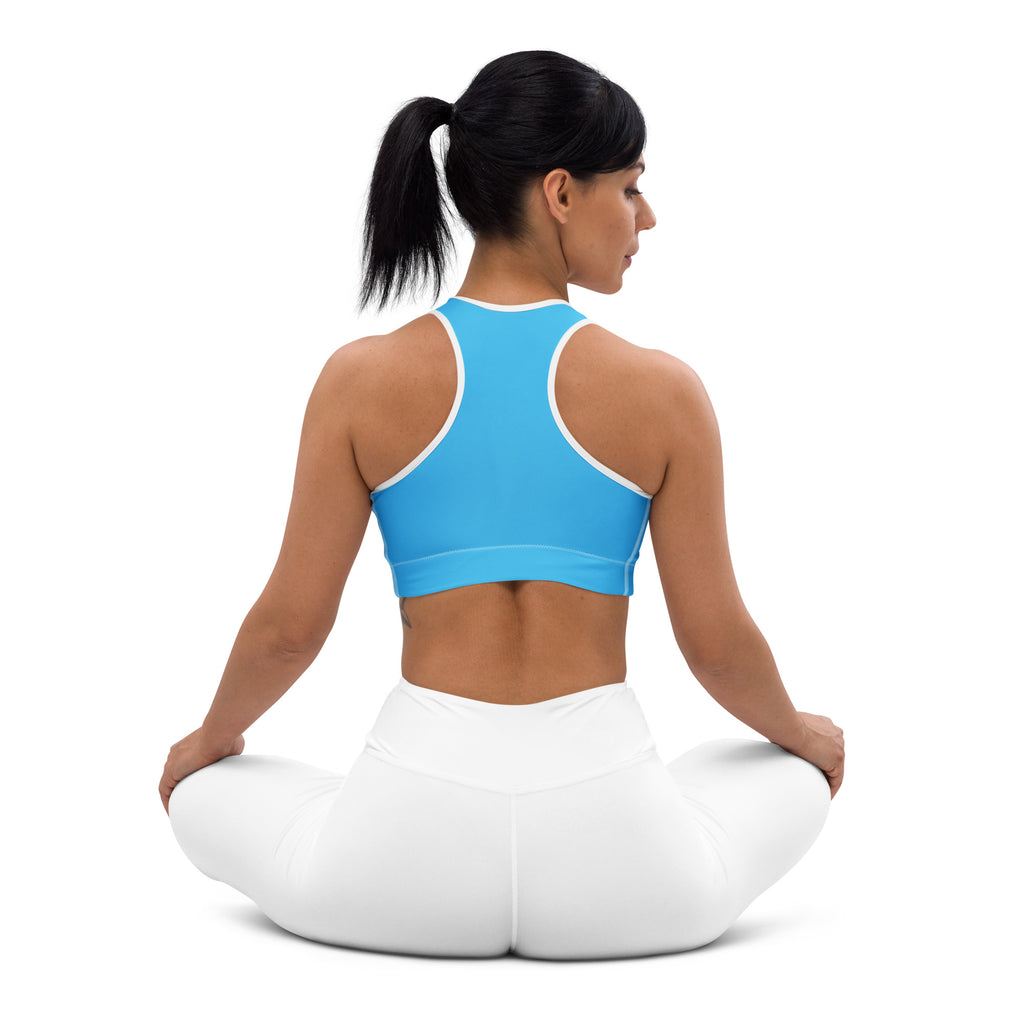 A woman wearing a women’s sky blue padded sports bra with white trim and white leggings seated in a yoga pose