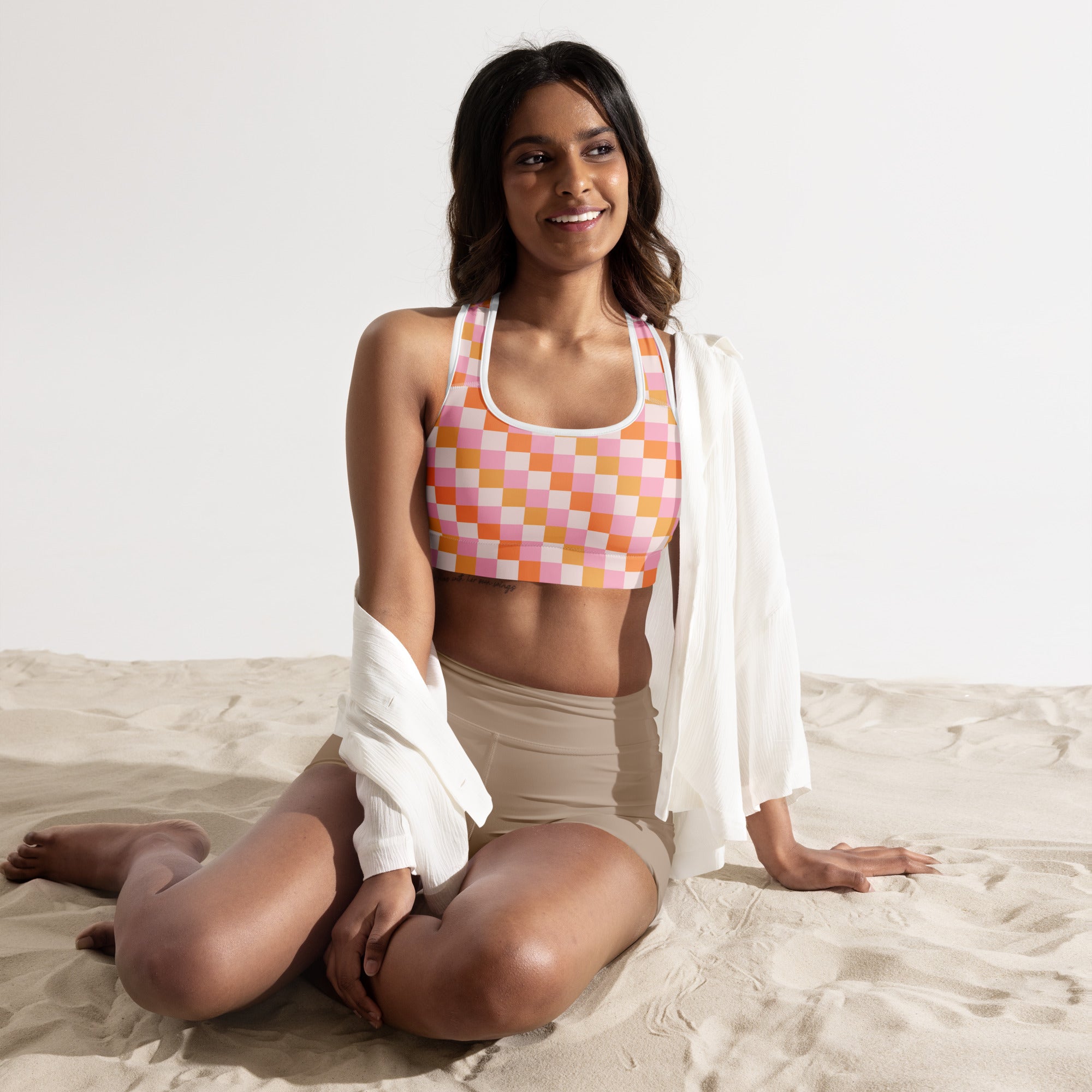 A woman wearing a buttery soft pink and orange checkerboard padded sports bra with white trim and quick-dry fabric
