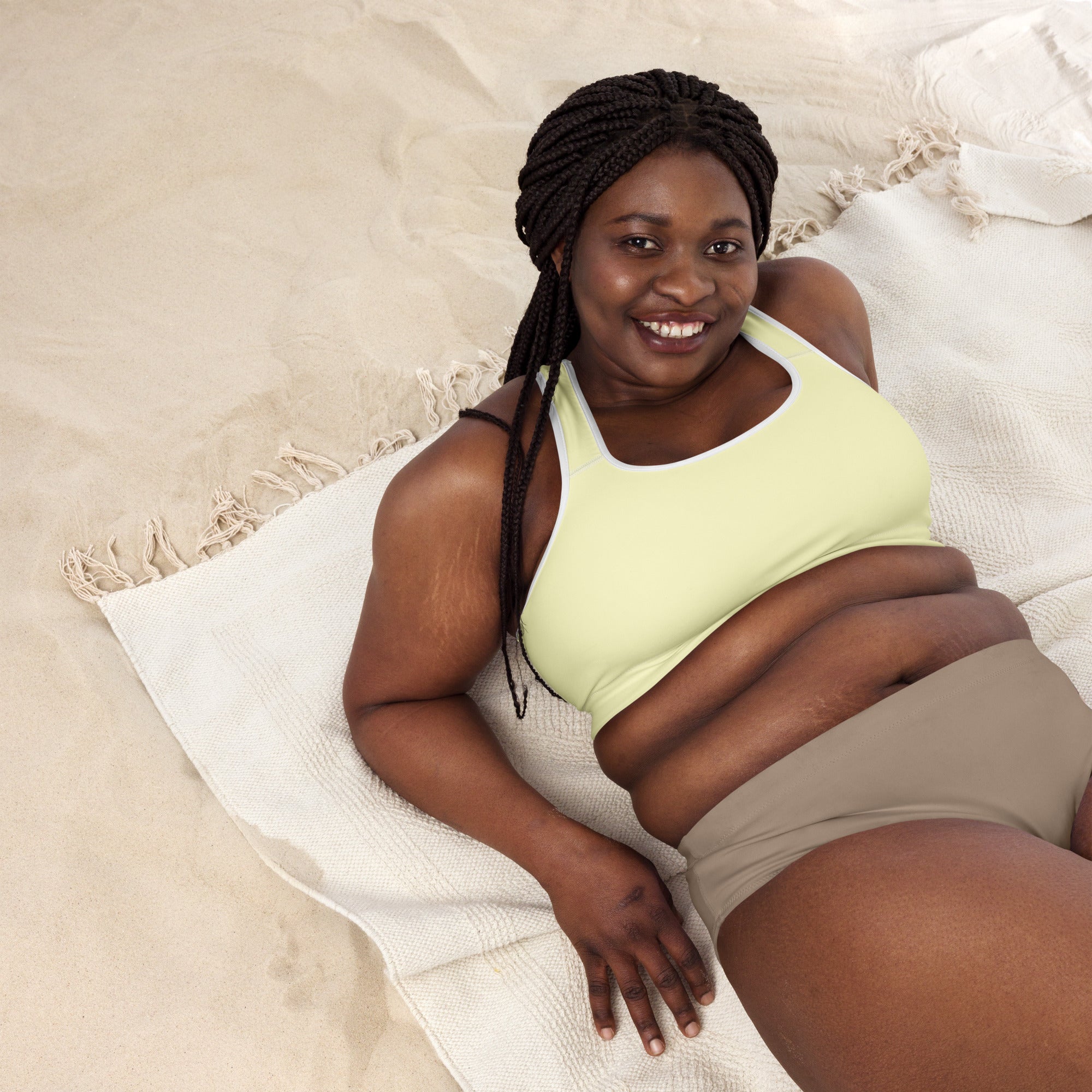 A woman lying on a towel wearing a light green sports bra with thin black straps and beige shorts