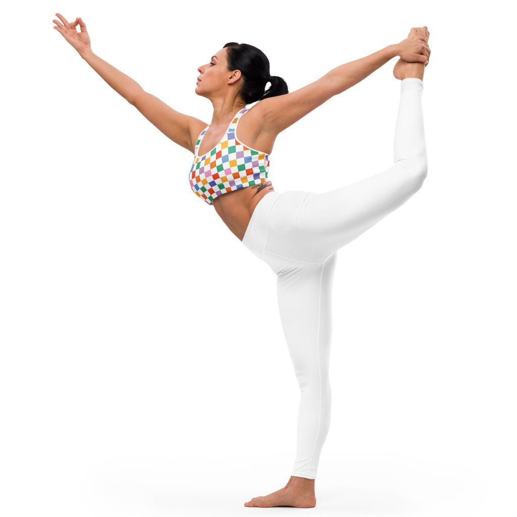 A woman wearing a colorful checkerboard padded sports bra and white leggings performs a yoga pose