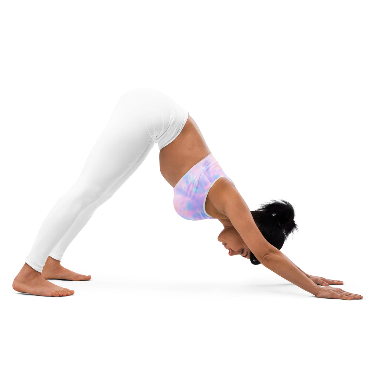 A woman in a pastel tie-dye watercolor padded sports bra and white leggings performs downward dog yoga pose