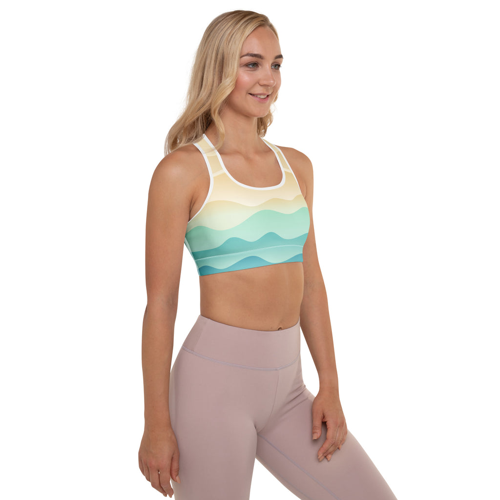 A woman wears a womens pastel ocean wave padded sports bra in buttery soft fabric with yellow mint green and teal waves