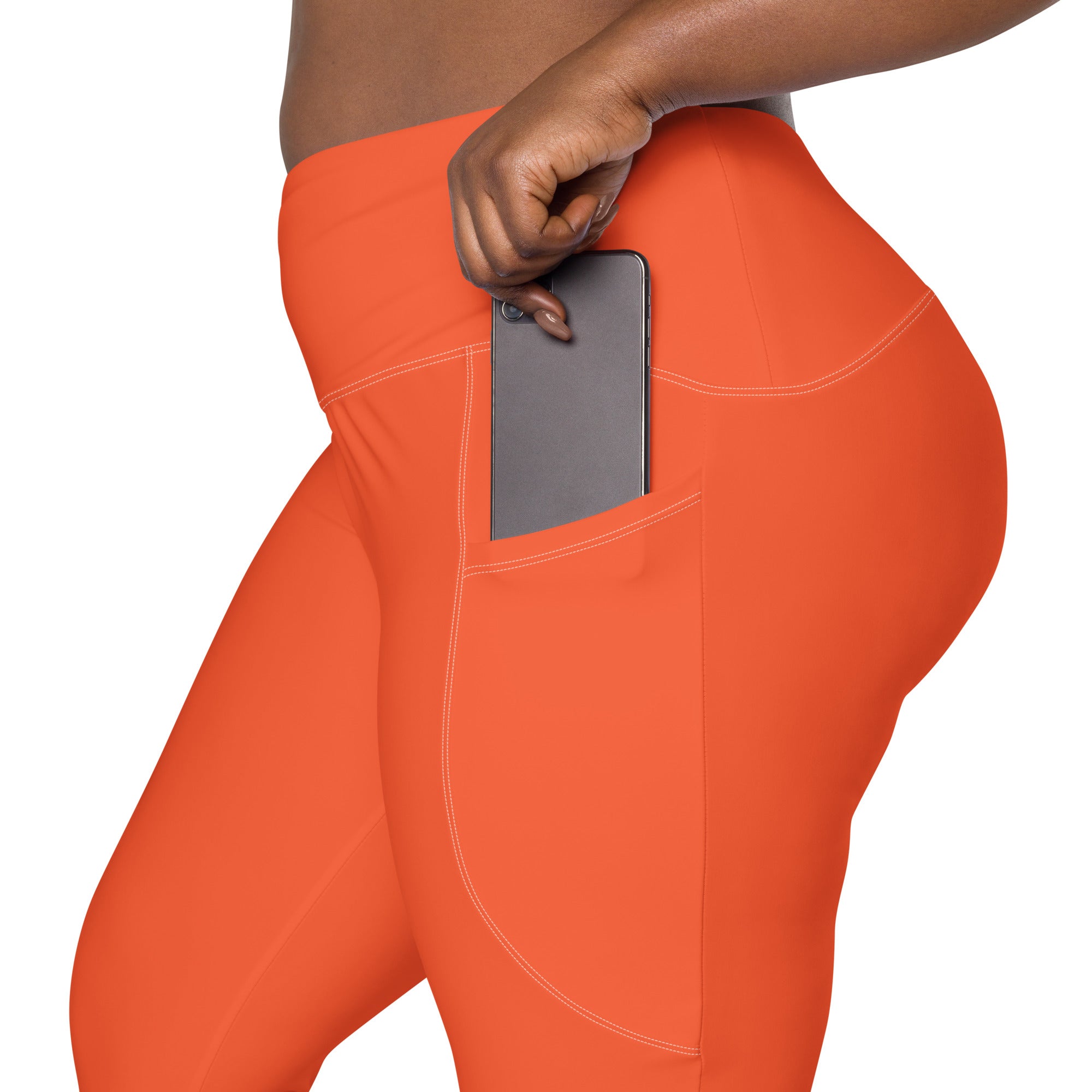 Women’s bright orange high-waisted yoga leggings with soft compression fabric and side pocket holding a smartphone