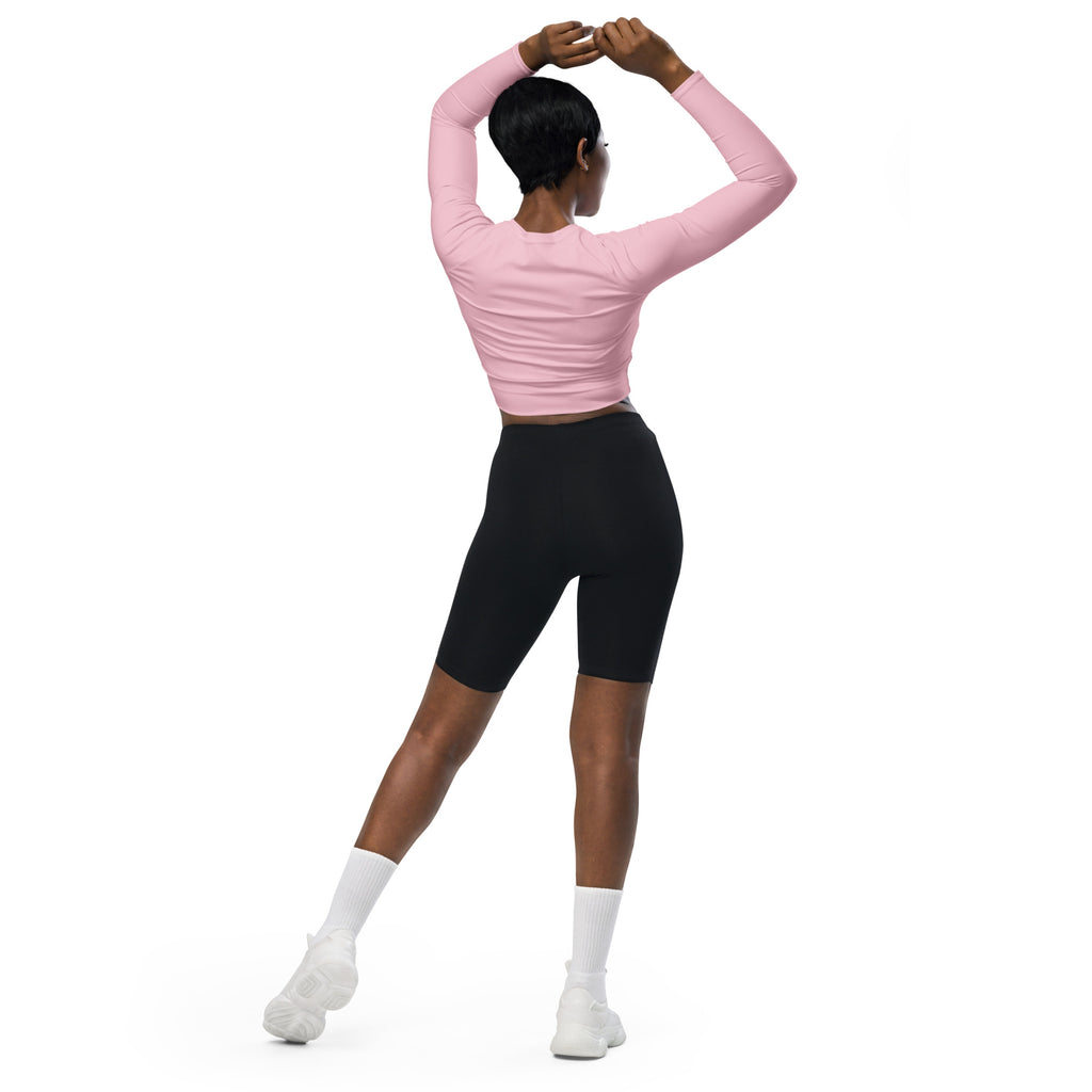 A woman wearing a women’s light pink long sleeve performance crop top in pink with black biker shorts