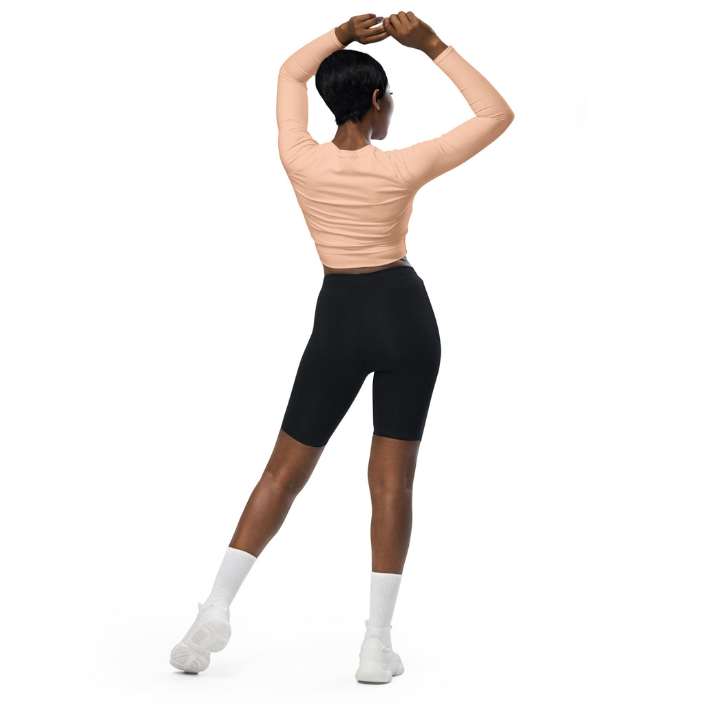 A woman wearing a women’s peach long sleeve performance crop top with black biker shorts