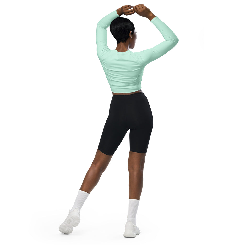 A woman wearing a women’s mint green long sleeve performance crop top with black biker shorts
