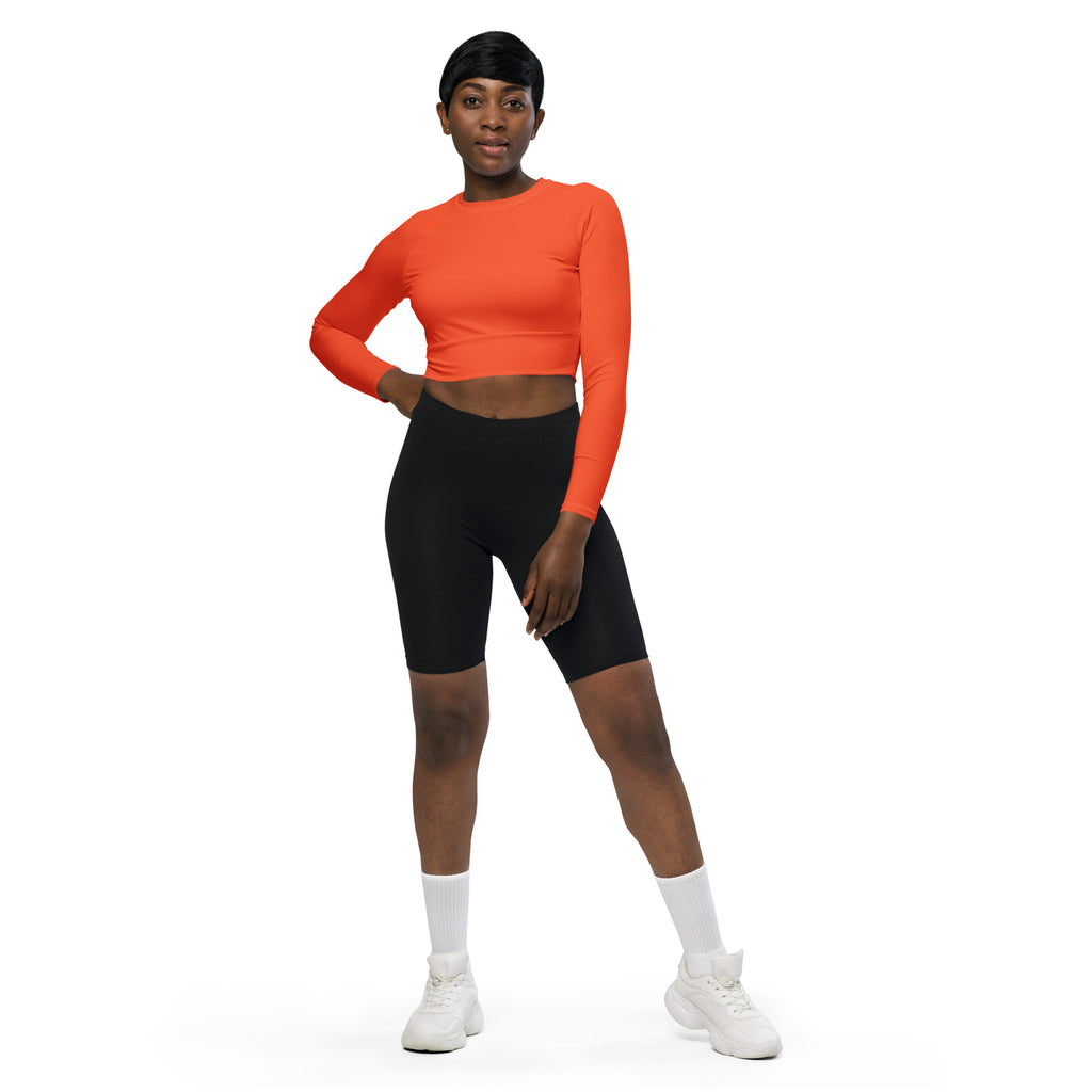 A woman wears a vibrant orange long sleeve performance crop top paired with black biker shorts and white shoes
