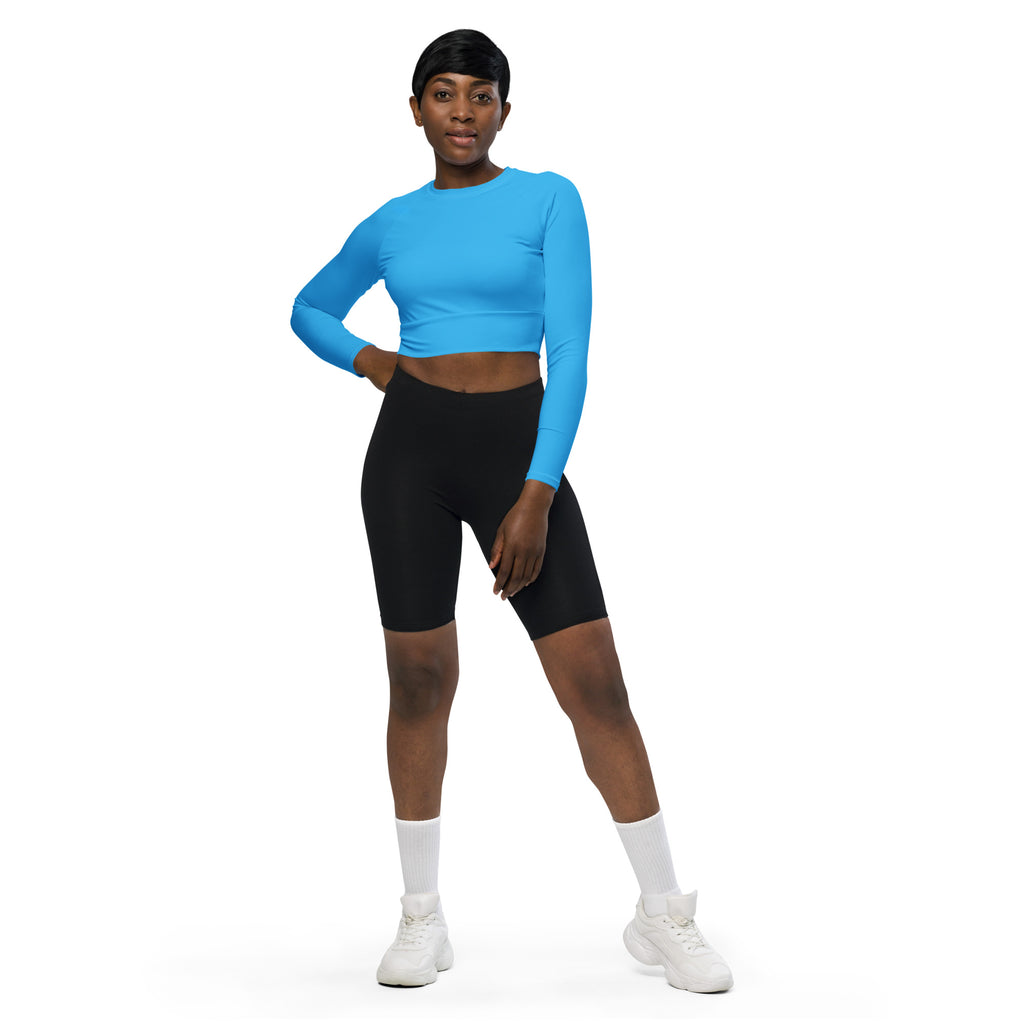 A woman wearing a sky blue long sleeve performance crop top with black biker shorts and white athletic shoes