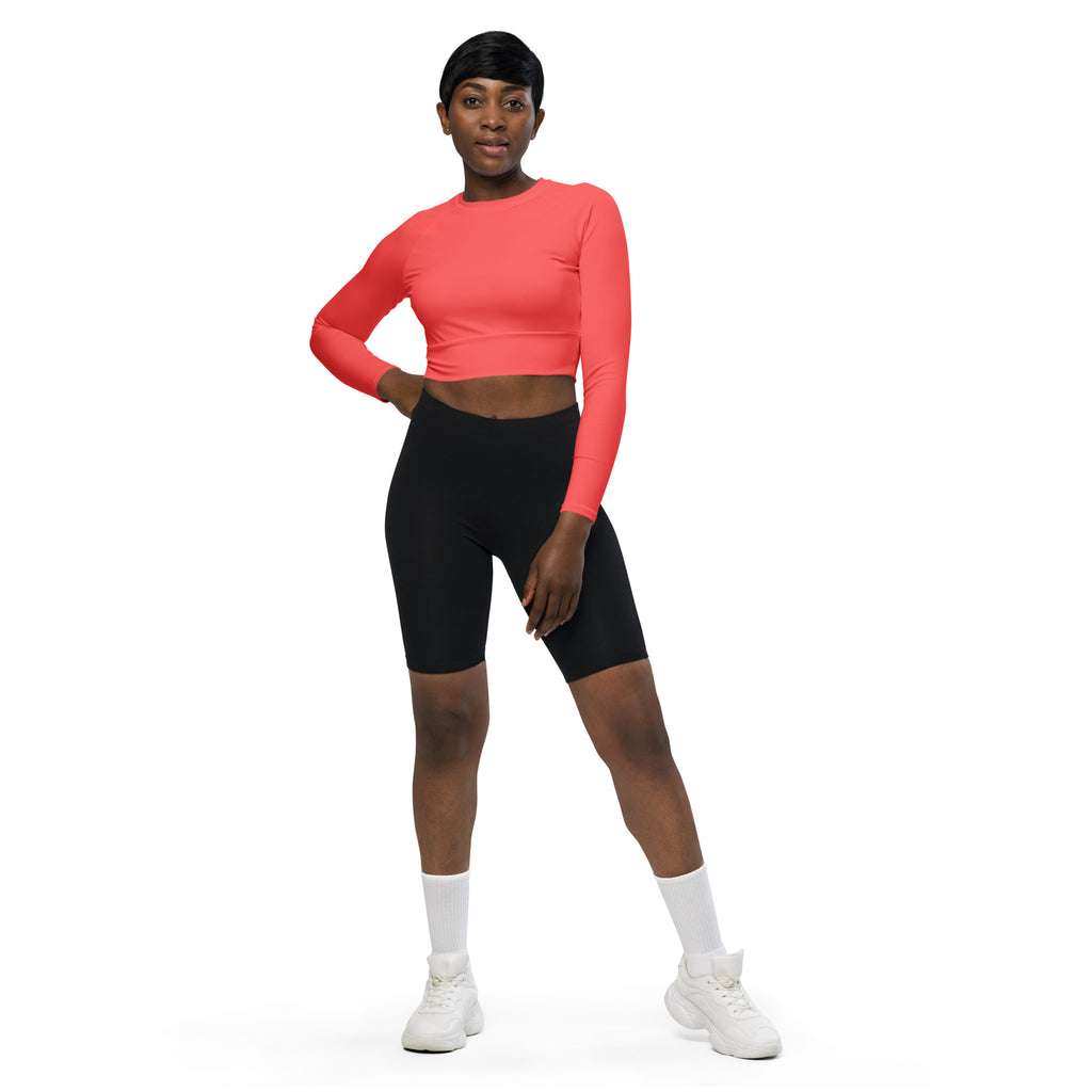 A woman wearing a women’s coral long sleeve performance crop top with black biker shorts from the front view