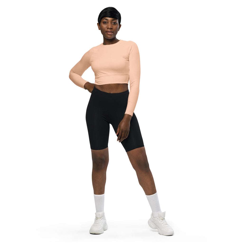 A woman wearing a women’s peach long sleeve performance crop top with black biker shorts in a fitness setting