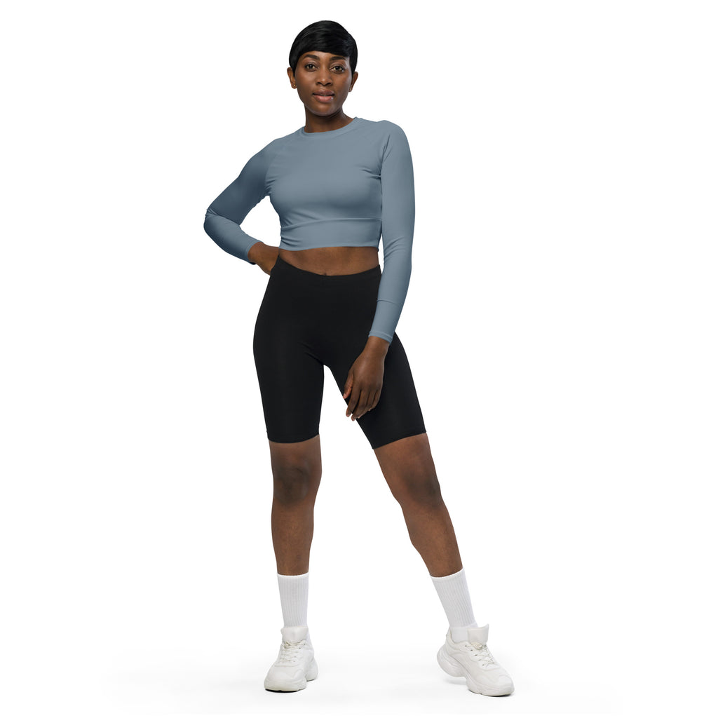 A woman wearing a women’s slate blue long sleeve performance crop top with black biker shorts facing forward