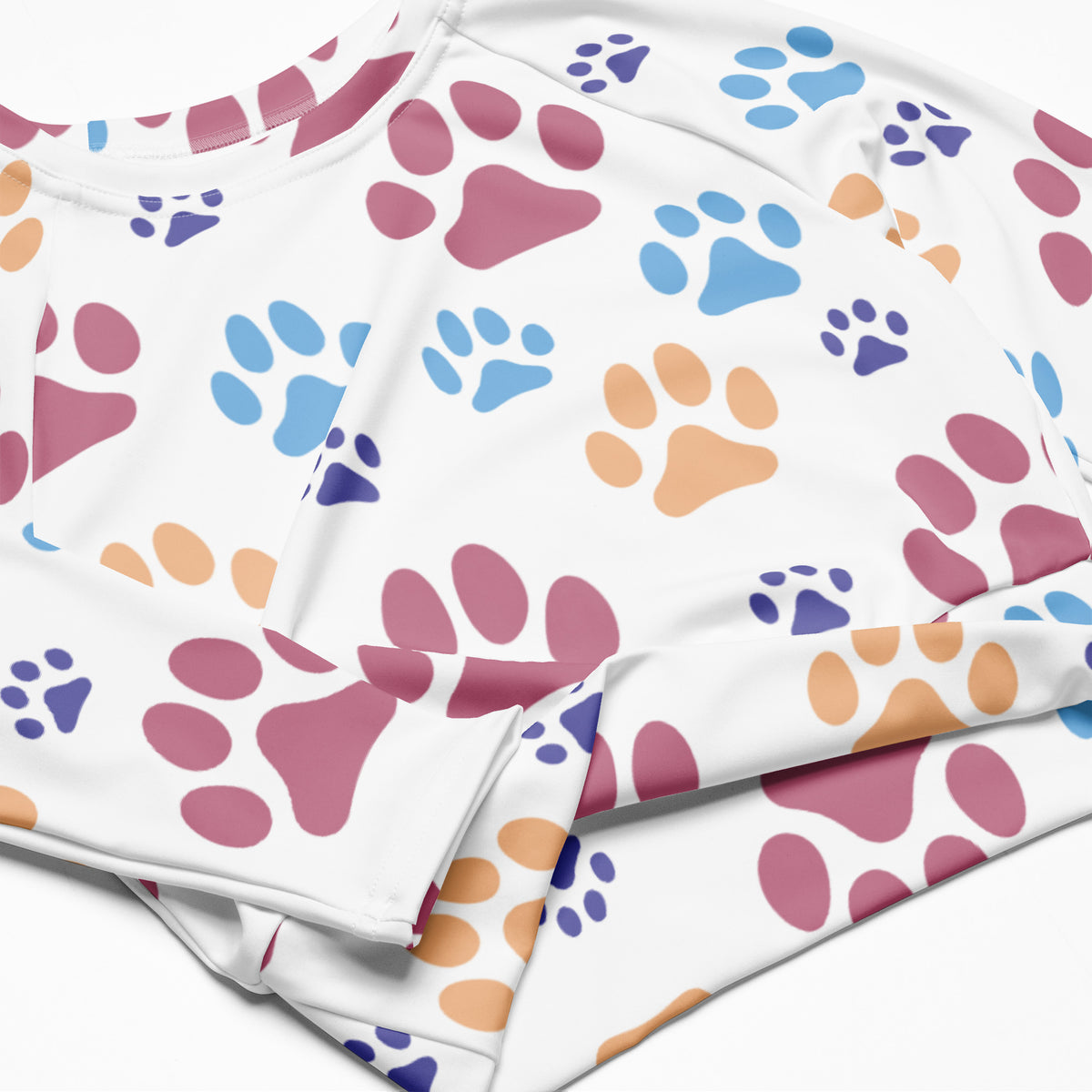 Women’s white long sleeve performance crop top with colorful pink blue and orange paw print pattern