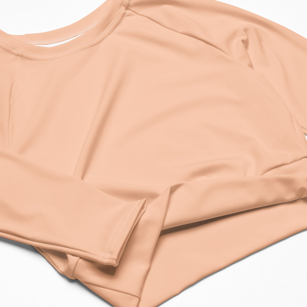 A women’s peach long sleeve performance crop top with smooth stretchy fabric and a simple round neckline