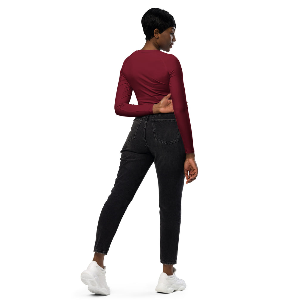 A woman wears a fitted maroon long sleeve performance crop top paired with dark wash skinny jeans and white sneakers