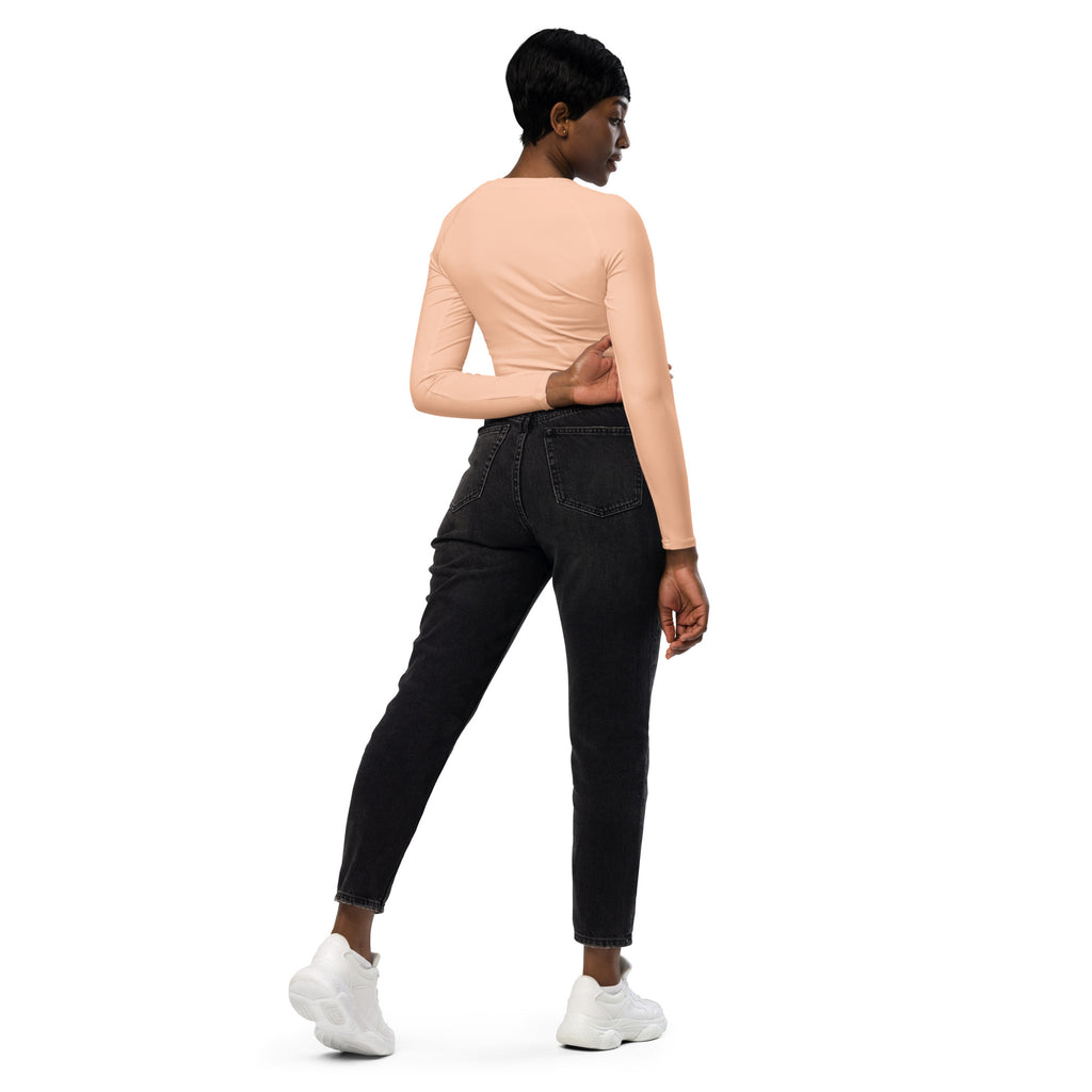 A woman wearing a peach long sleeve performance crop top and black high waisted jeans showcasing the front side