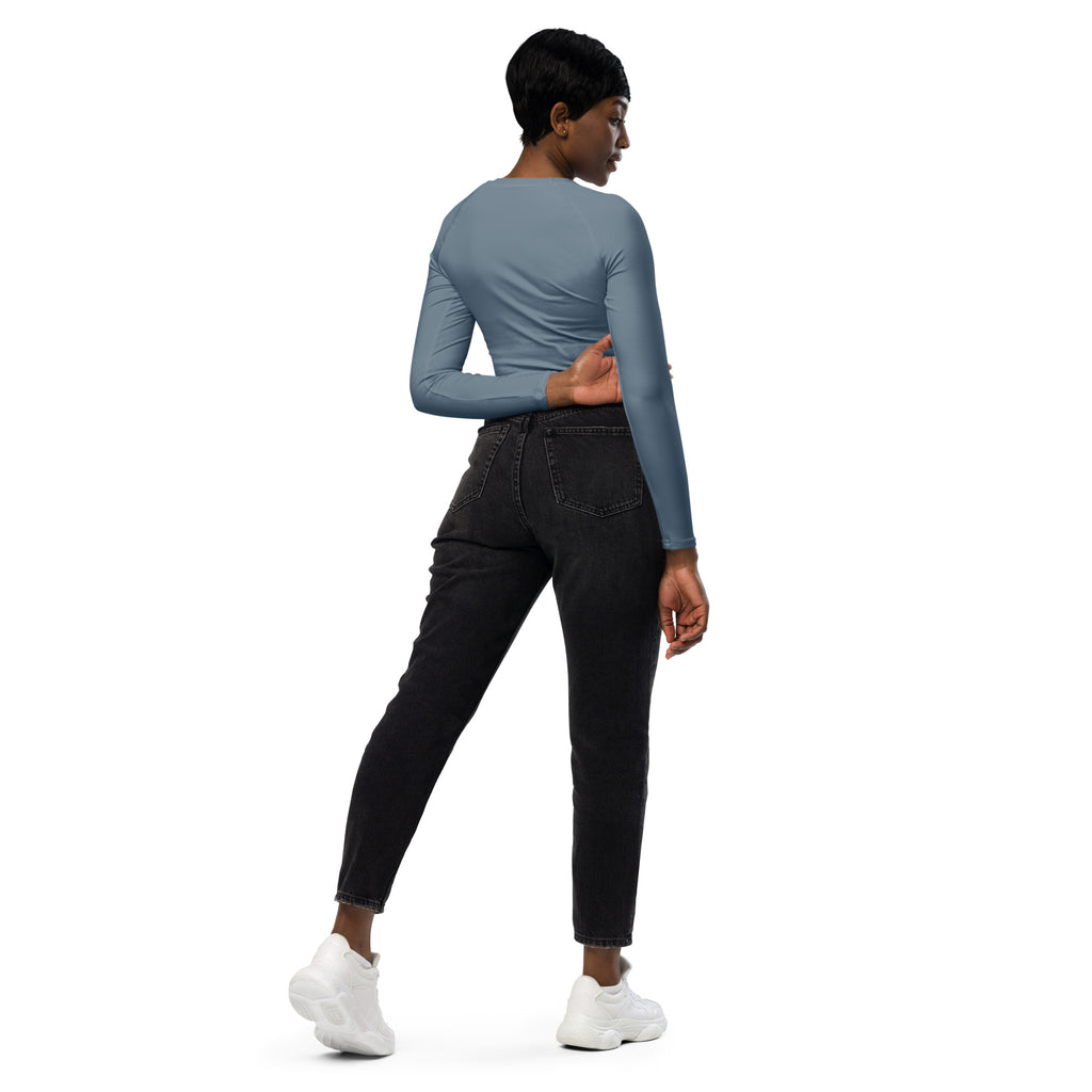 A woman wearing a fitted women’s slate blue long sleeve performance crop top with dark wash skinny jeans