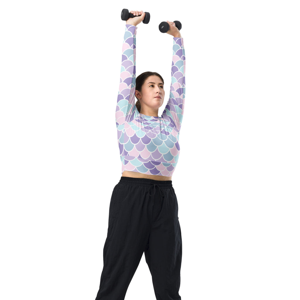 A woman wearing a women’s pastel mermaid scales long sleeve performance crop top in lavender light blue and pink