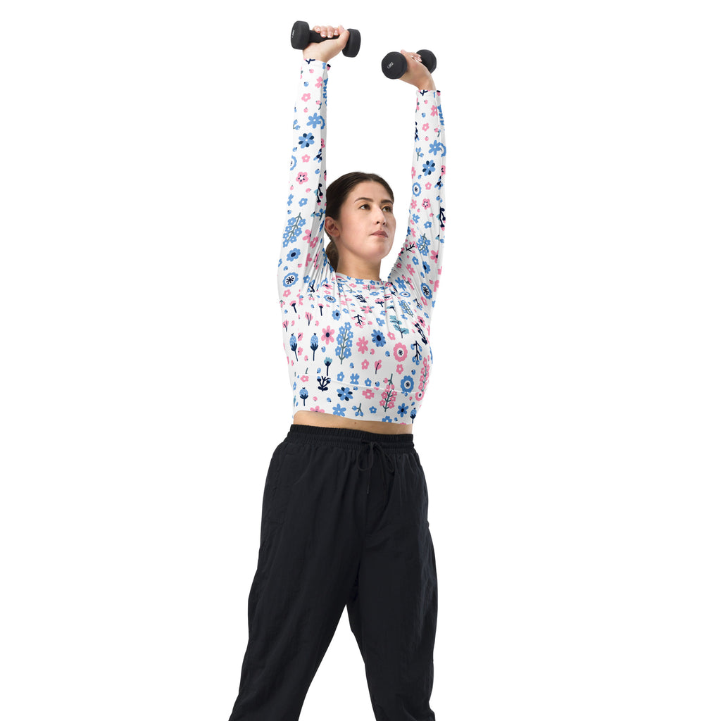 A woman lifting black dumbbells wearing a white pastel floral print long sleeve performance crop top