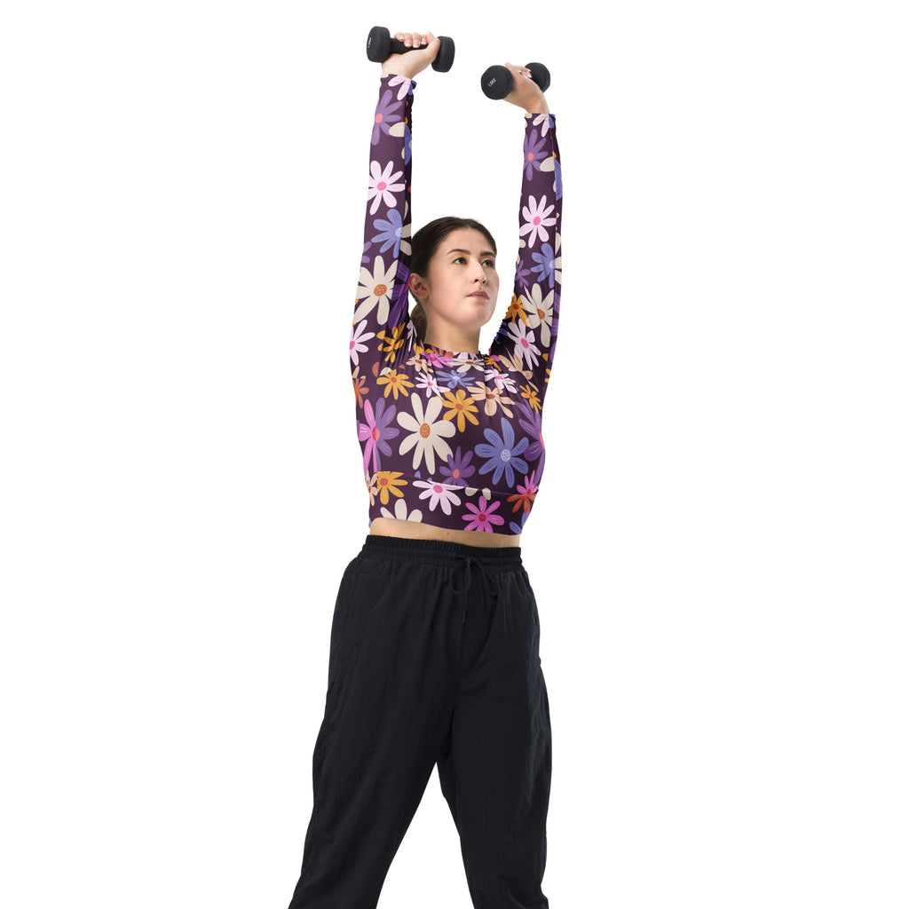 A woman holding black dumbbells overhead wearing a women’s purple floral long sleeve performance crop top