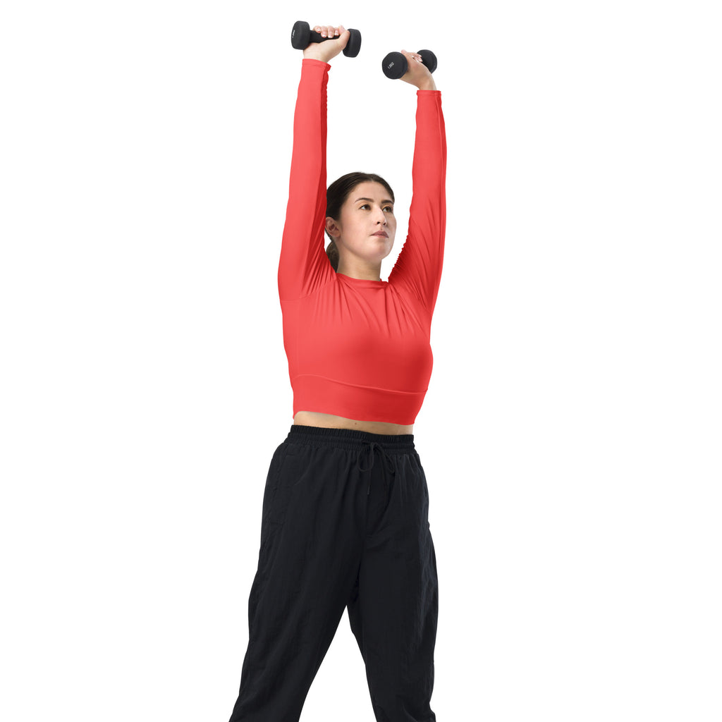 A woman wearing a women’s coral long sleeve performance crop top holds black dumbbells above her head
