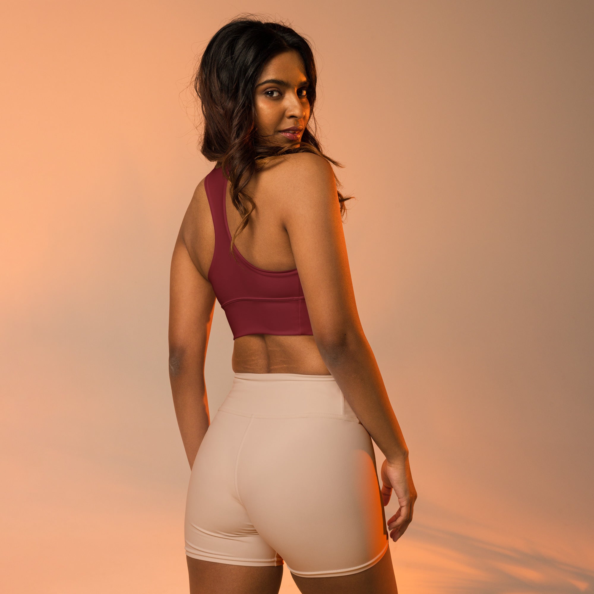Women’s buttery soft deep red recycled longline sports bra with racerback design paired with high waisted beige shorts